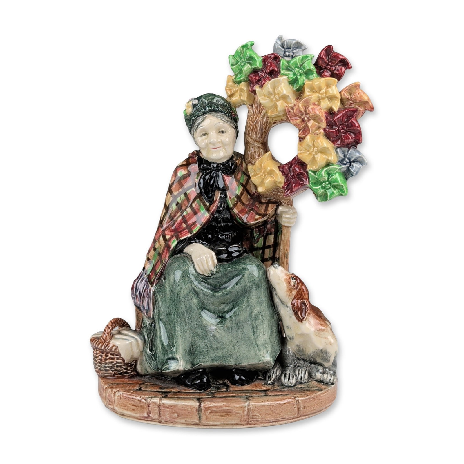 Royal Doulton Ceramic Figurine, The Windmills Lady HN1400: Designed by Leslie Harradine. The figure depicts an elderly woman in a plaid shawl and green skirt seated on a bench next to a small dog, holding a circular arrangement of multi-colored pinwheels. The