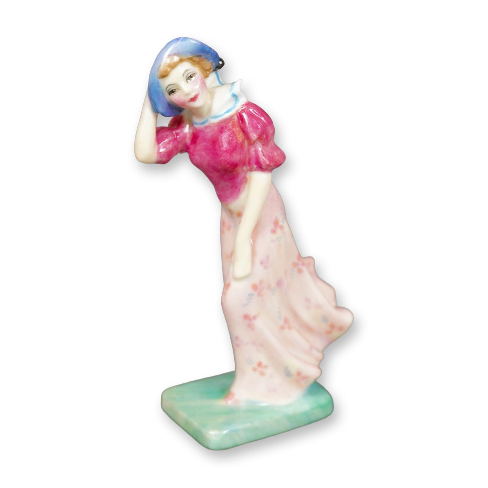 Royal Doulton Bone China Figurine, Windflower M78: Hand painted figure of a young woman in a floral pink dress and light-purple hat. She is shown standing against the wind. Royal Doulton backstamp. Dimensions: 2.5"L x 1.25"W x 4.25"H Manufacturer or B