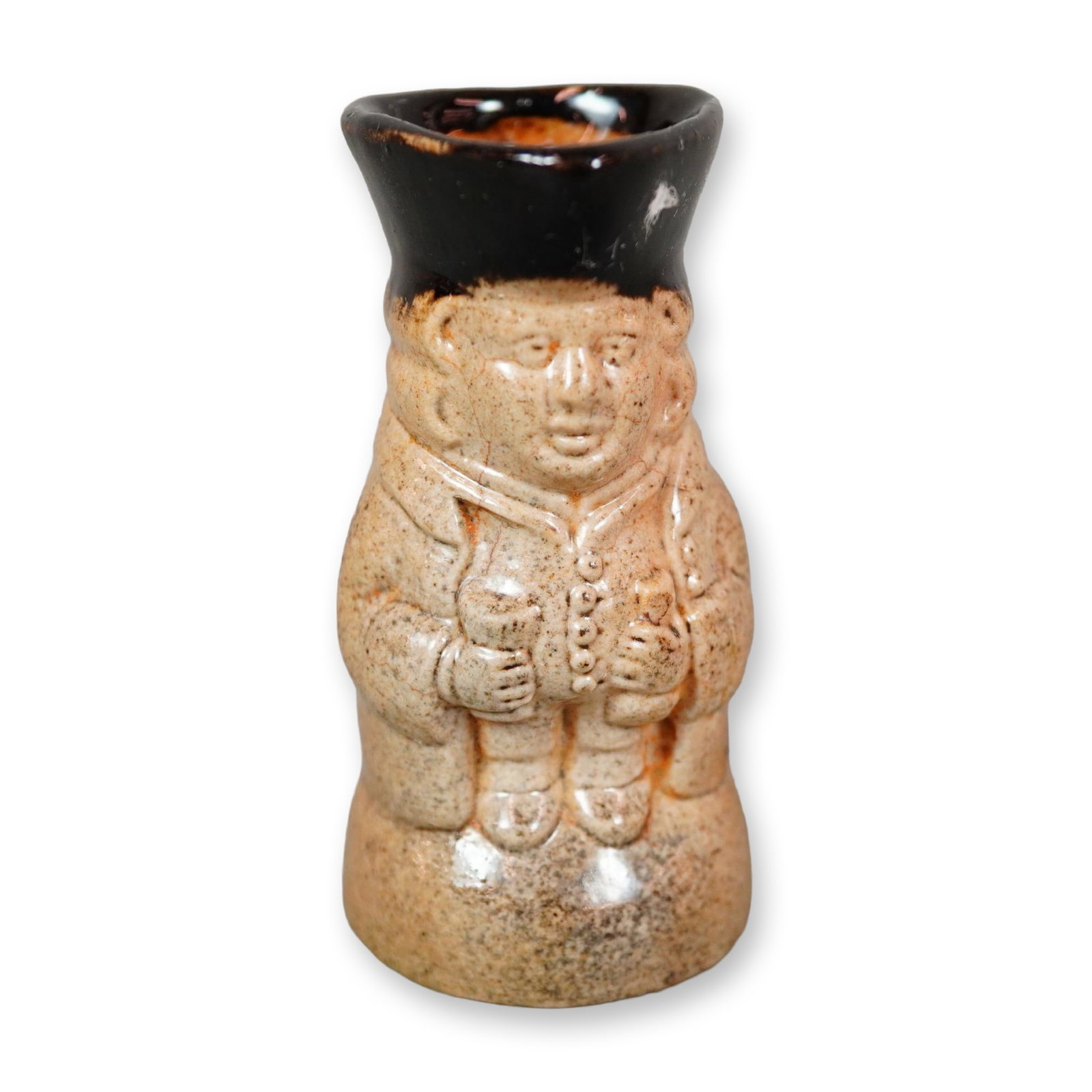 Doulton Lambeth Stoneware Salt-Glazed Standing Toby Jug: A figural jug depicting a standing man, with a somber face, holding a beaker and mug of ale. The body is finished in a salt-glazed style, while the hat and upper handle are highlighted in a glossy bla