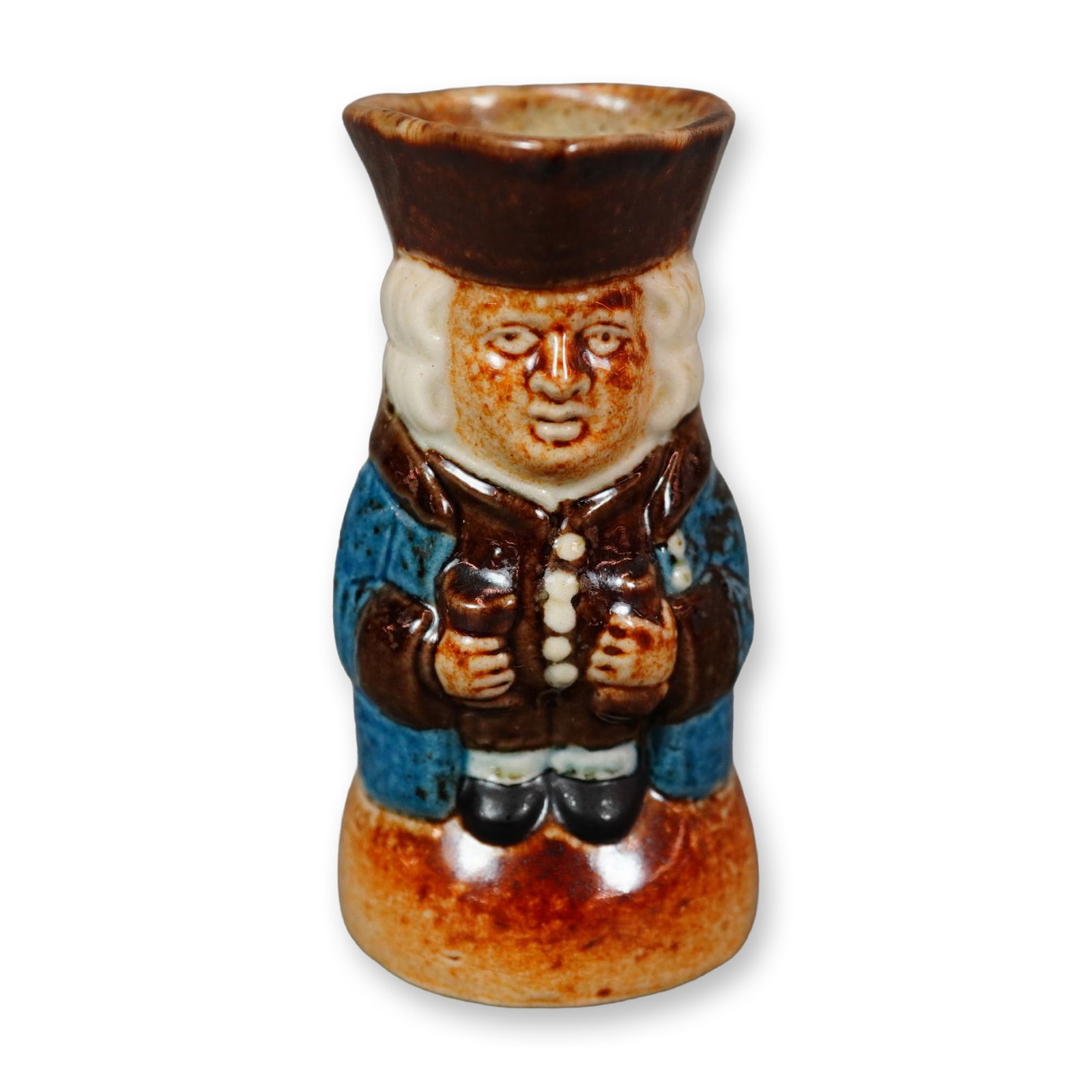 Royal Doulton Lambeth Stoneware Salt-Glazed Standing Toby Jug: A figural jug modeled as a standing gentleman with a solemn expression, holding a beaker and a mug of ale. Rendered in a salt-glazed finish, the figure wears a glossy blue coat with brown accents, a w