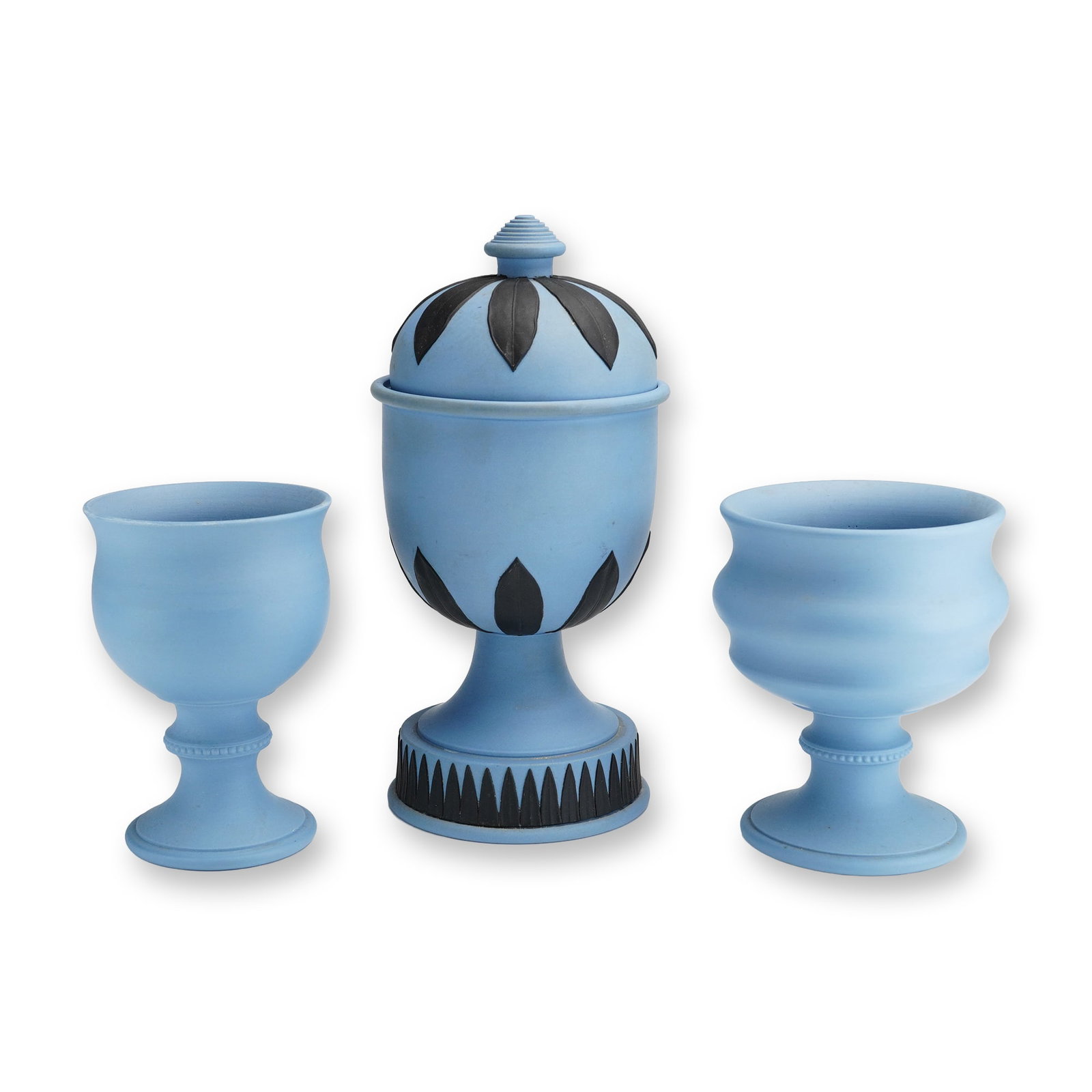 Three Wedgwood England Blue Jasperware Lidded Urn and Coupes: Wedgwood, England. Trio of blue jasperware vessels including one lidded urn and two footed coupes. The ovoid urn is decorated with black sprigged foliate motifs and a geometric band at the pedestal ba