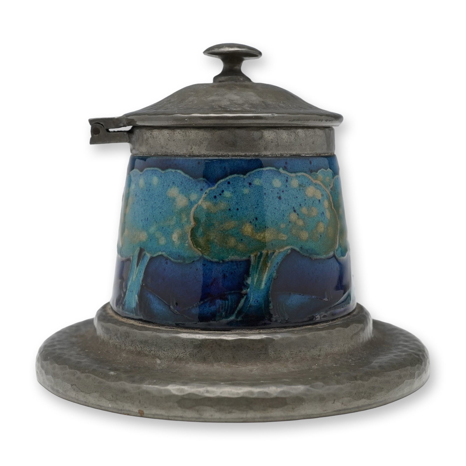 Moorcroft Pottery For Liberty & Co. Tudric Pewter Inkwell, Moonlit Blue: A inkwell comprising a Tudric hammered pewter base and hinged lid, enclosing a tube lined decorated holder. Depicts a band of stylized trees against a cobalt and indigo ground. Tudric Moorcroft and 01
