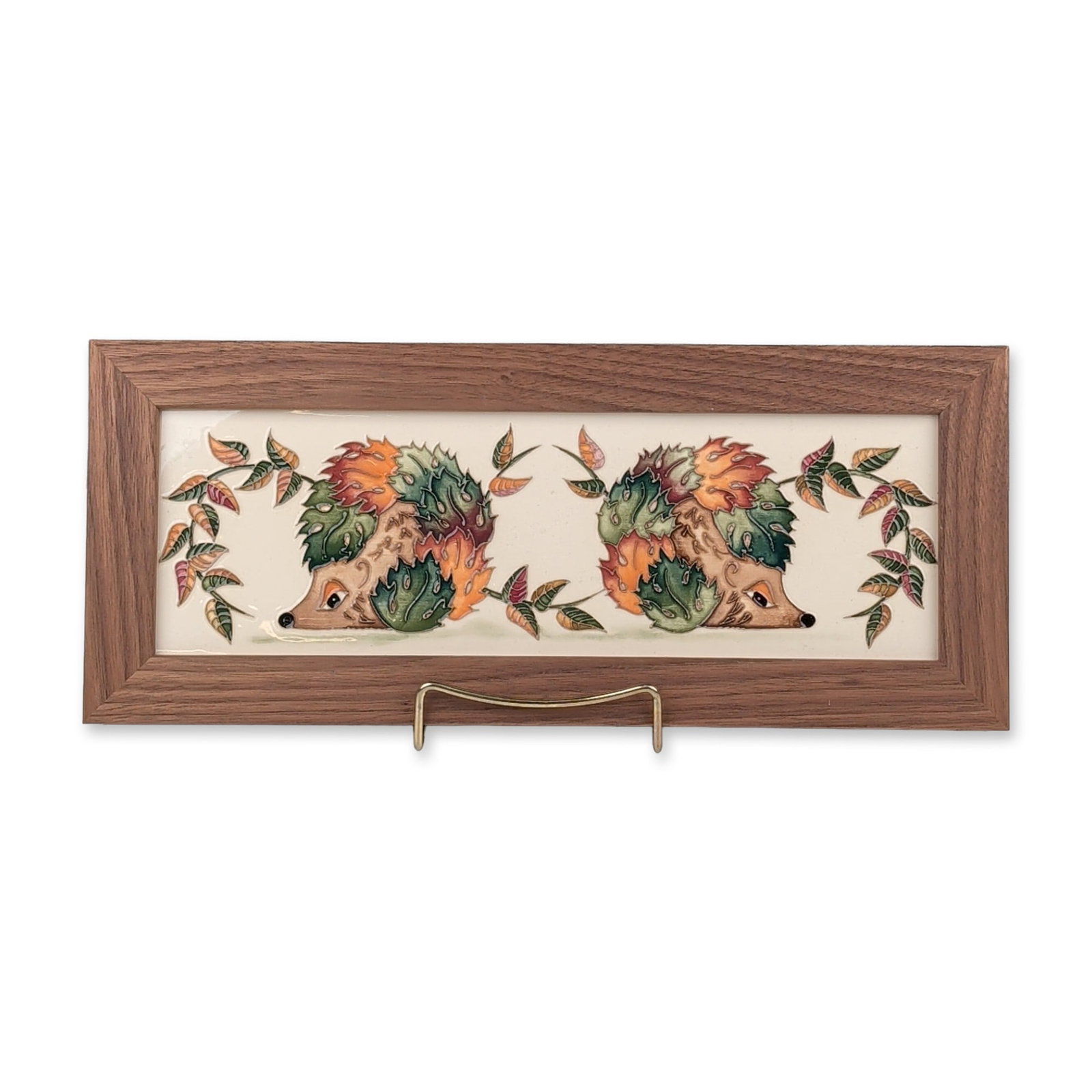 Moorcroft Pottery Framed Hedgehog and Autumn Leaves Tile: Limited edition. Rectangular ceramic plaque in tube-lined earthenware, featuring a design of two hedgehogs nestled among stylized autumnal leaves in shades of green, rust orange, and burgundy on a cre