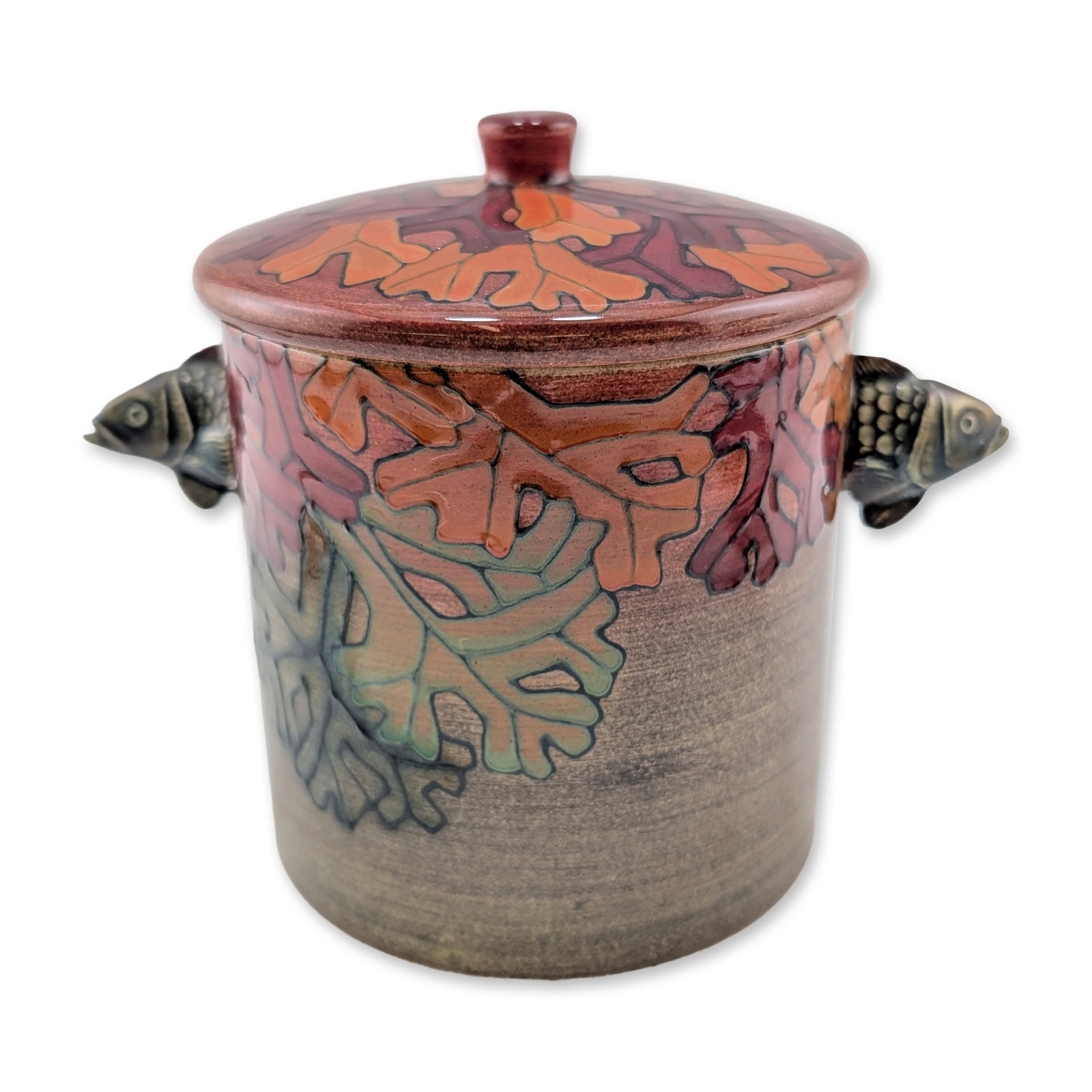 Dennis Chinaworks by Sally Tuffin Lidded Fish Head Handle Jar: The cylindrical form features tube-lined foliate decoration of overlapping coral in shades of russet, orange, and sage green against a speckled gray-brown ground. Two applied handles are modeled as fi