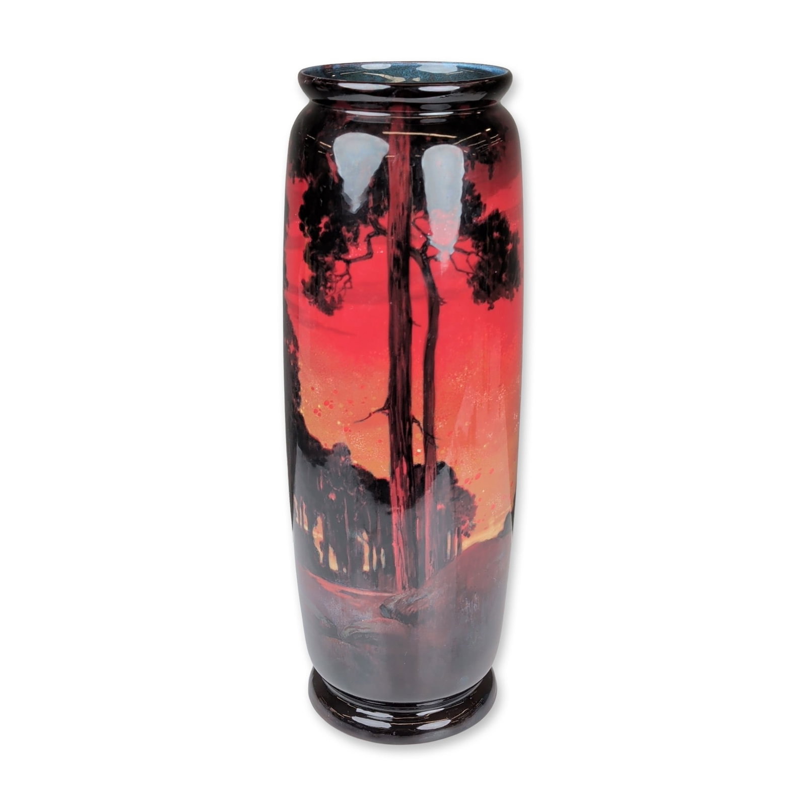 Royal Doulton by Charles Noke Flambe Sung Landscape Vase: A tall cylindrical earthenware vase featuring a wooded landscape decoration with silhouetted trees against a vibrant red and orange flambe glaze. The interior of the rim is finished with a mottled blu