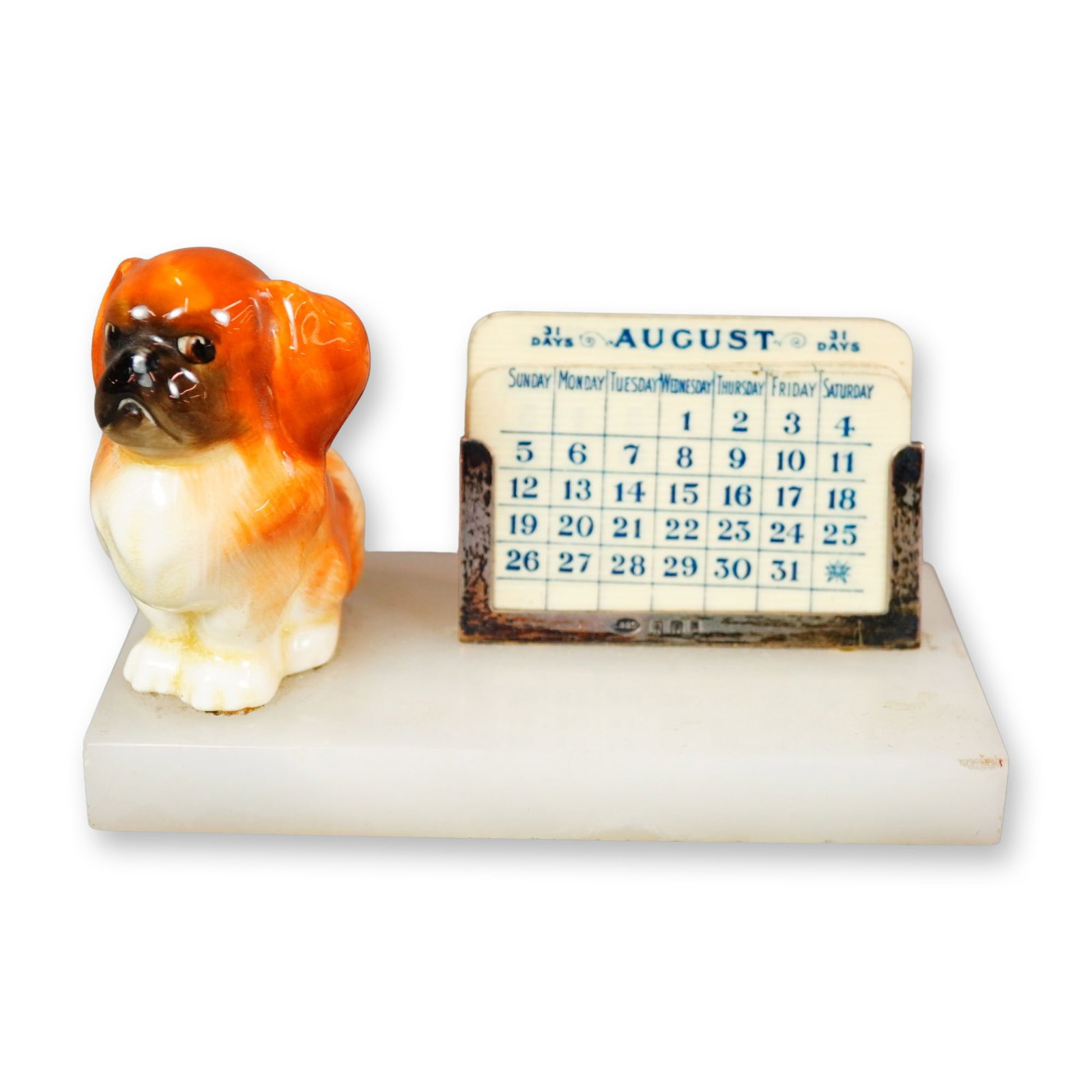 Royal Doulton Porcelain and Sterling Silver Onyx Desk Calendar, Pekinese Puppy Seated HN832: A hand-painted Royal Doulton figurine of a brown and white Pekinese puppy seated on a white onyx base, positioned beside a set of celluloid calendar cards housed in a sterling silver holder by George 