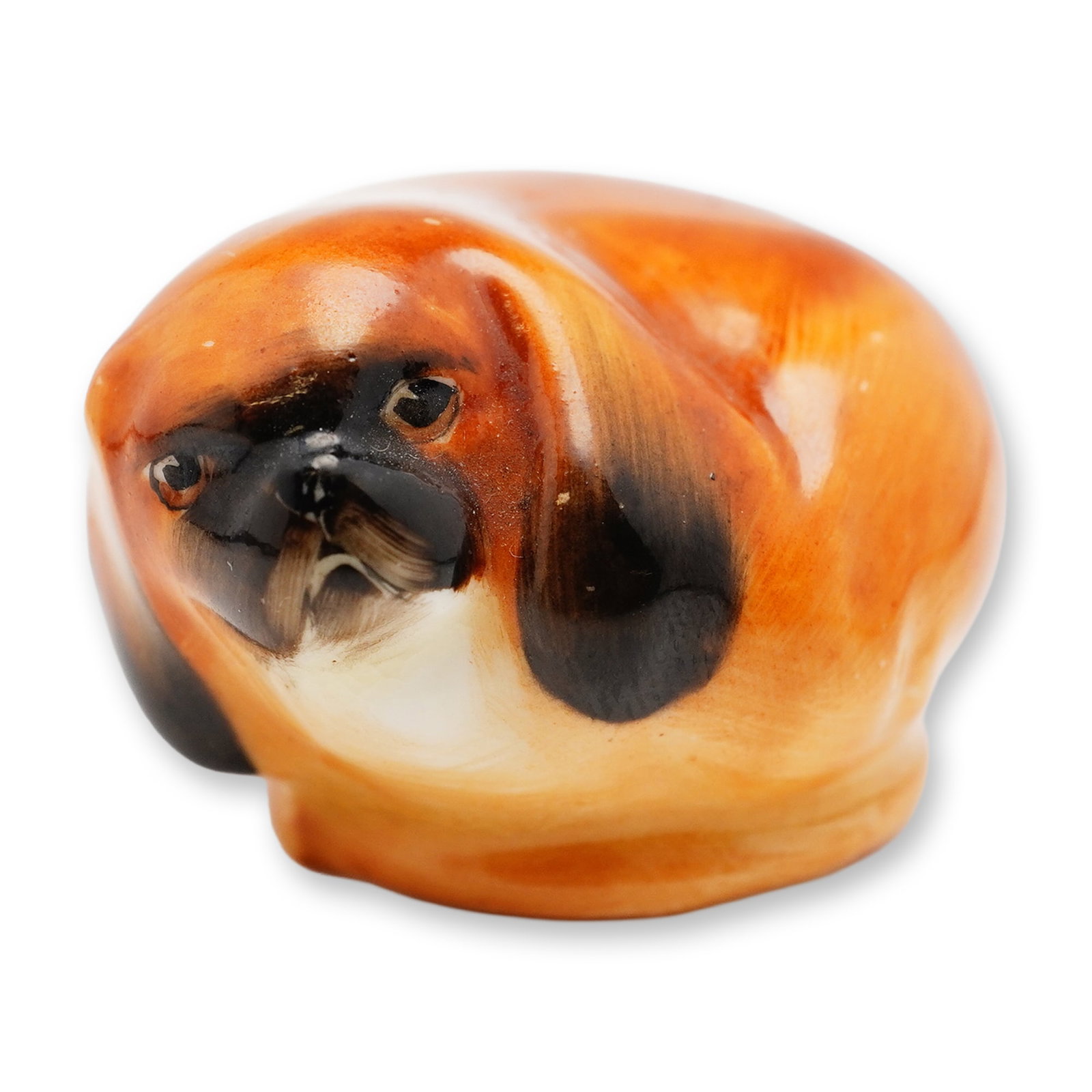 Doulton Porcelain Figurine, Pekinese Puppy Curled HN834: A small figurine of a Pekinese dog, featuring a brown coat with black detailing on the nose and ear tips. Doulton marked. Dimensions: 1.5"L x 1.25"W x 1"H Manufacturer or Brand: Doulton Country of Ori
