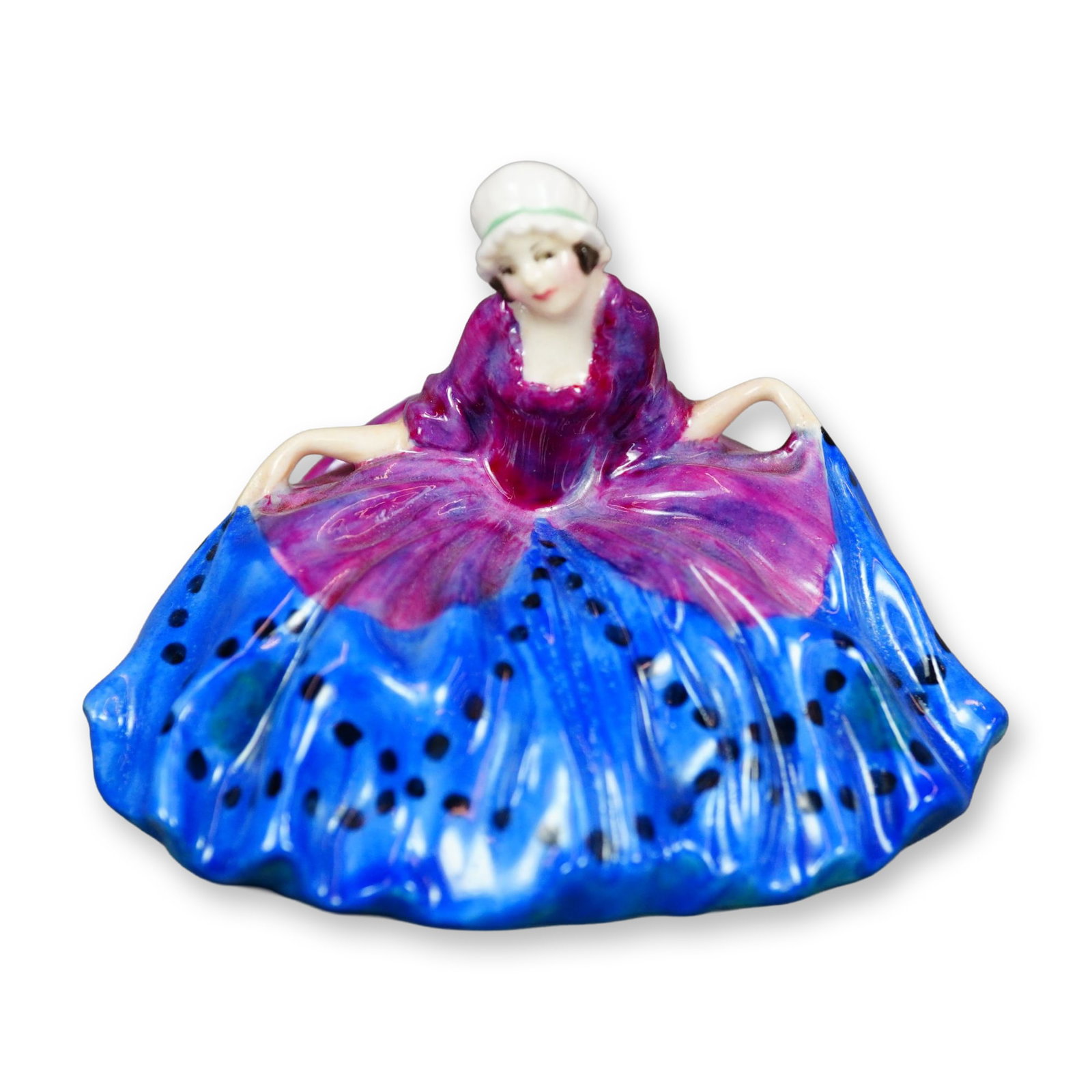 Royal Doulton Figurine, Polly Peachum M022: Character from "The Beggar's Opera", the figure depicts a young woman curtsying. She is shown wearing a blue and purple gown with black spot. Royal Doulton backstamp. Dimensions: 3"L x 2.5"W x 2.25"H 