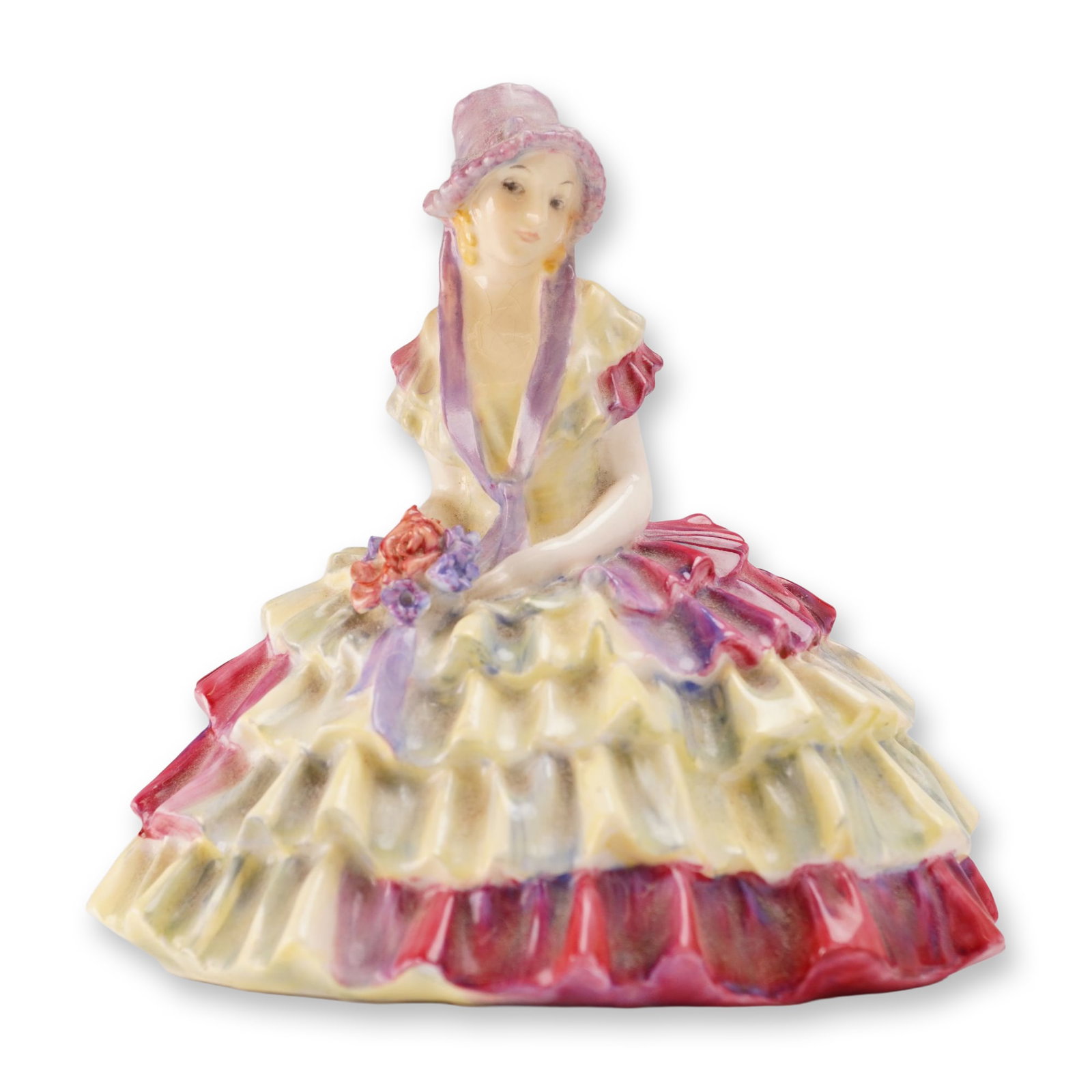 Royal Doulton Porcelain Figurine, Chloe HN1470: Designed by Leslie Harradine. The figure depicts a seated woman wearing a wide-brimmed pink hat and a multi-tiered ruffled crinoline dress decorated in pale yellow, deep rose, and purple, holding a sm