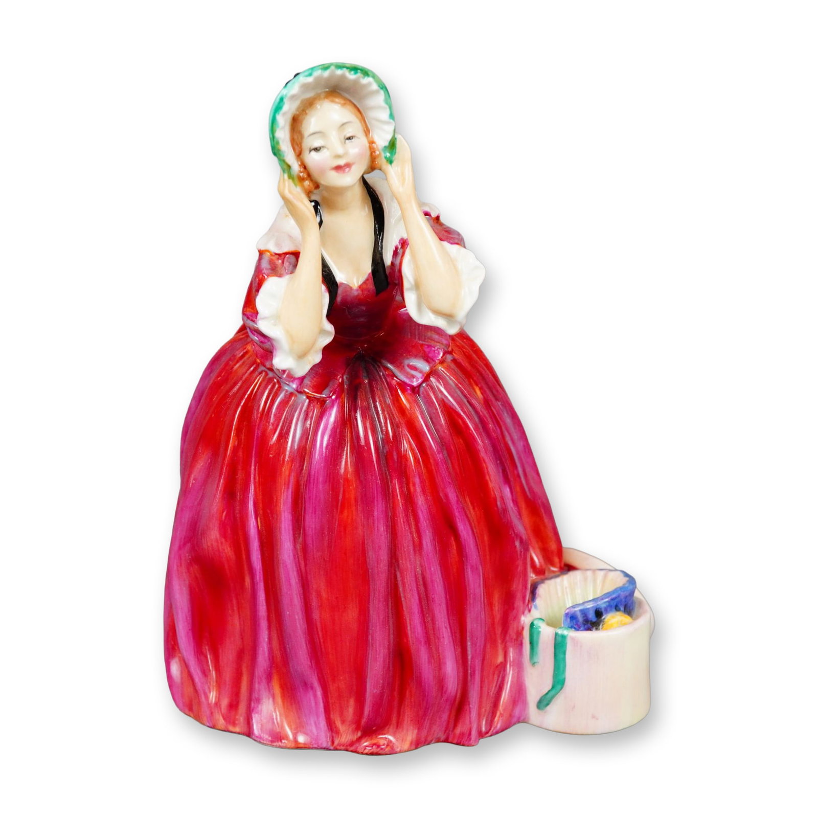 Royal Doulton Bone China Figurine, The Choice HN1959: Designed by Leslie Harradine, the figure depicts a young woman in a floor-length dress standing beside a hatbox and selecting from a group of bonnets. Royal Doulton backstamp. Signed by Michael Doulto