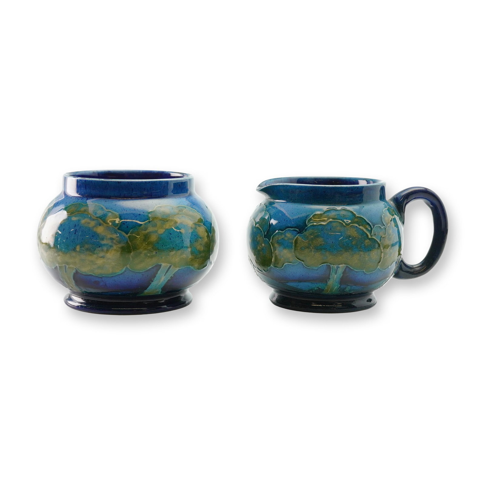 2pc Moorcroft Pottery Creamer and Sugar Bowl, Moonlit Blue: Creamer and sugar bowl which features a landscape motif with tube-lined outlines of trees against a cobalt blue background with light an medium blues and green glazes. Moorcroft impressed mark on base