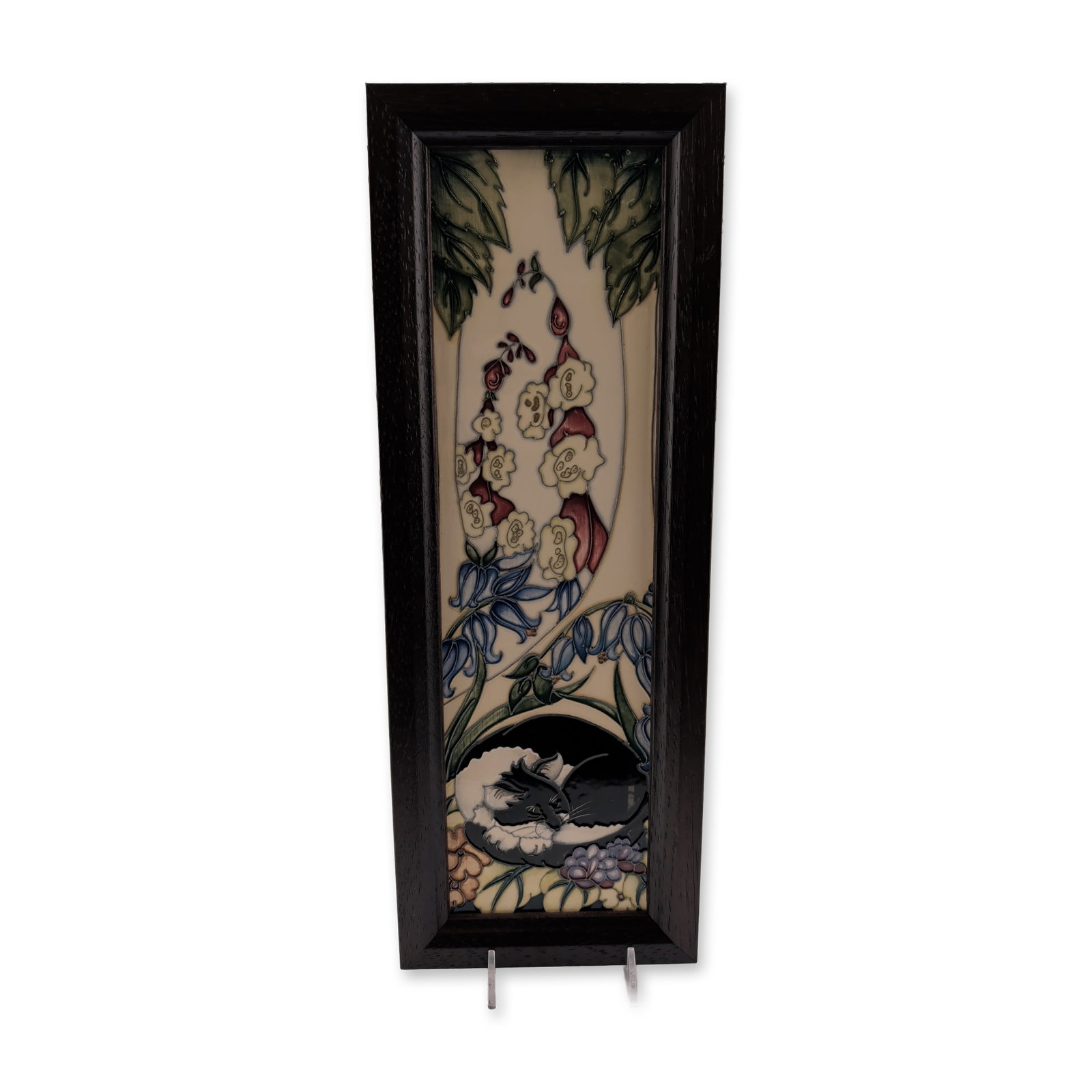 Framed Moorcroft Pottery by Rachel Bishop Ceramic Plaque, Catnap: Featuring a tube-lined design of a sleeping black and white cat nestled among foxgloves and bluebells. The decoration is finished in hand-painted gloss glazes over a cream ground. Housed in a dark-sta
