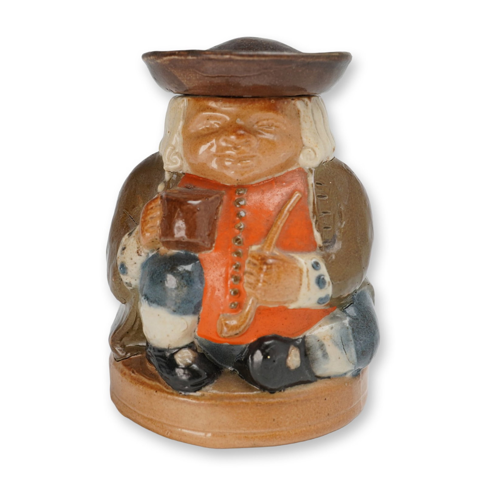 Royal Doulton Lambeth Stoneware Salt-Glazed Covered Ink Pot, Honest Measure: Jar with a removable lid formed by the figure's tricorn hat. The molded figure is depicted seated, wearing a brown hat, white wig, orange-red waistcoat, brown coat, and blue-gray breeches, holding a m
