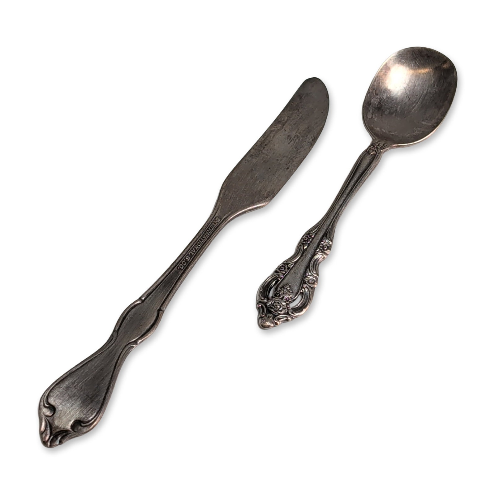 Two Oneida and International Silver-Plated Flatware Pieces: One Oneida Community silver-plated spoon in the Coronation pattern, introduced in 1936, featuring a pierced handle terminal with floral and scrollwork decoration. Marked Community on the reverse of
