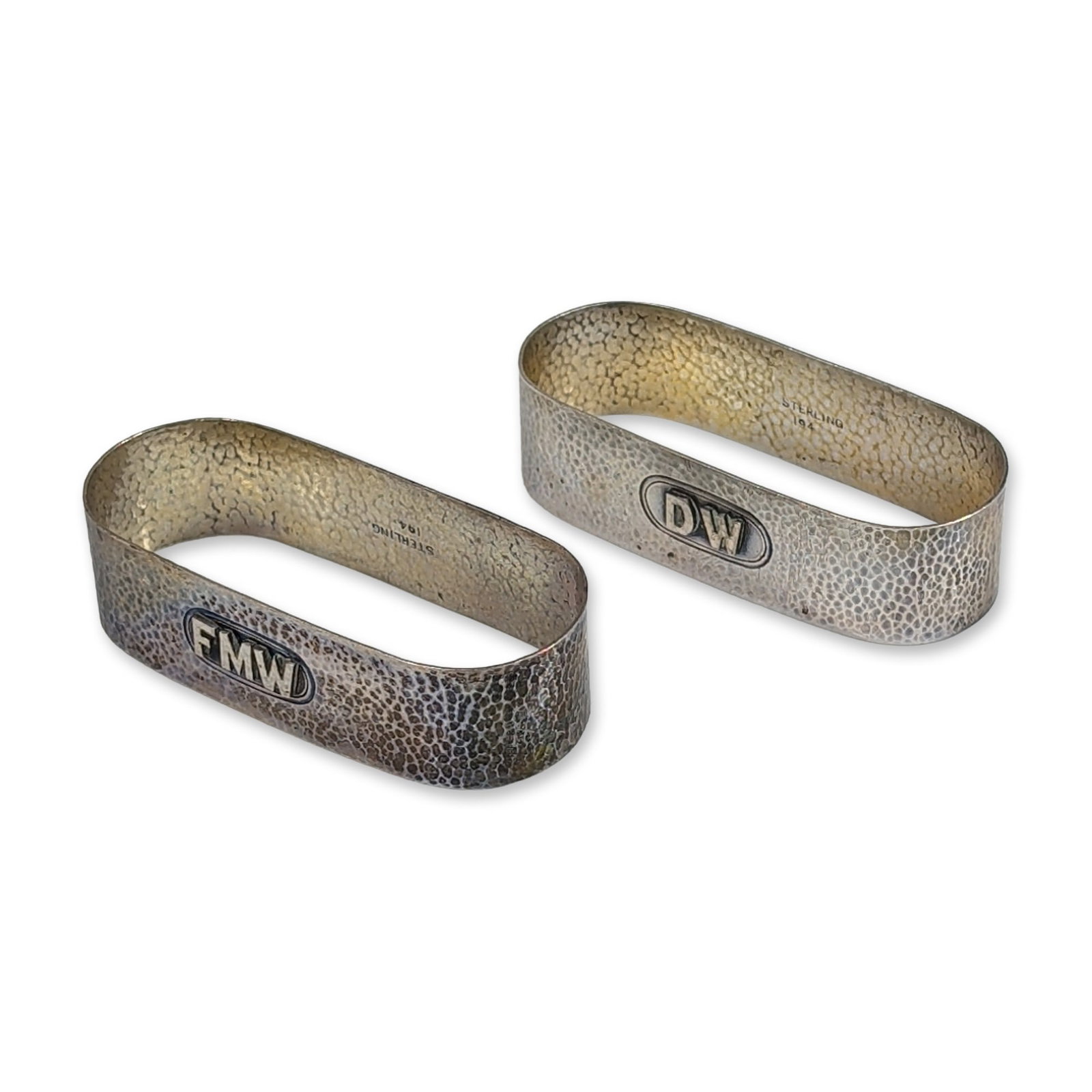 Pair of Sterling Silver Napkin Rings: Sterling silver napkin rings featuring hammered surfaces and applied block-letter monograms. One ring is monogrammed DW and the other FMW. The interior of each ring is stamped STERLING and 194. Two