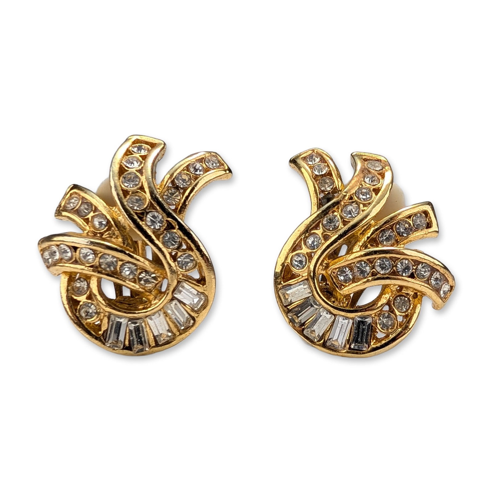 Pair of Gold Toned Rhinestone Swirl Clip Earrings: A pair of vintage gold-toned clip-on costume jewelry earrings. The design features a dynamic abstract swirl or plume motif. The earrings are embellished with pave-set round-cut clear rhinestones and a