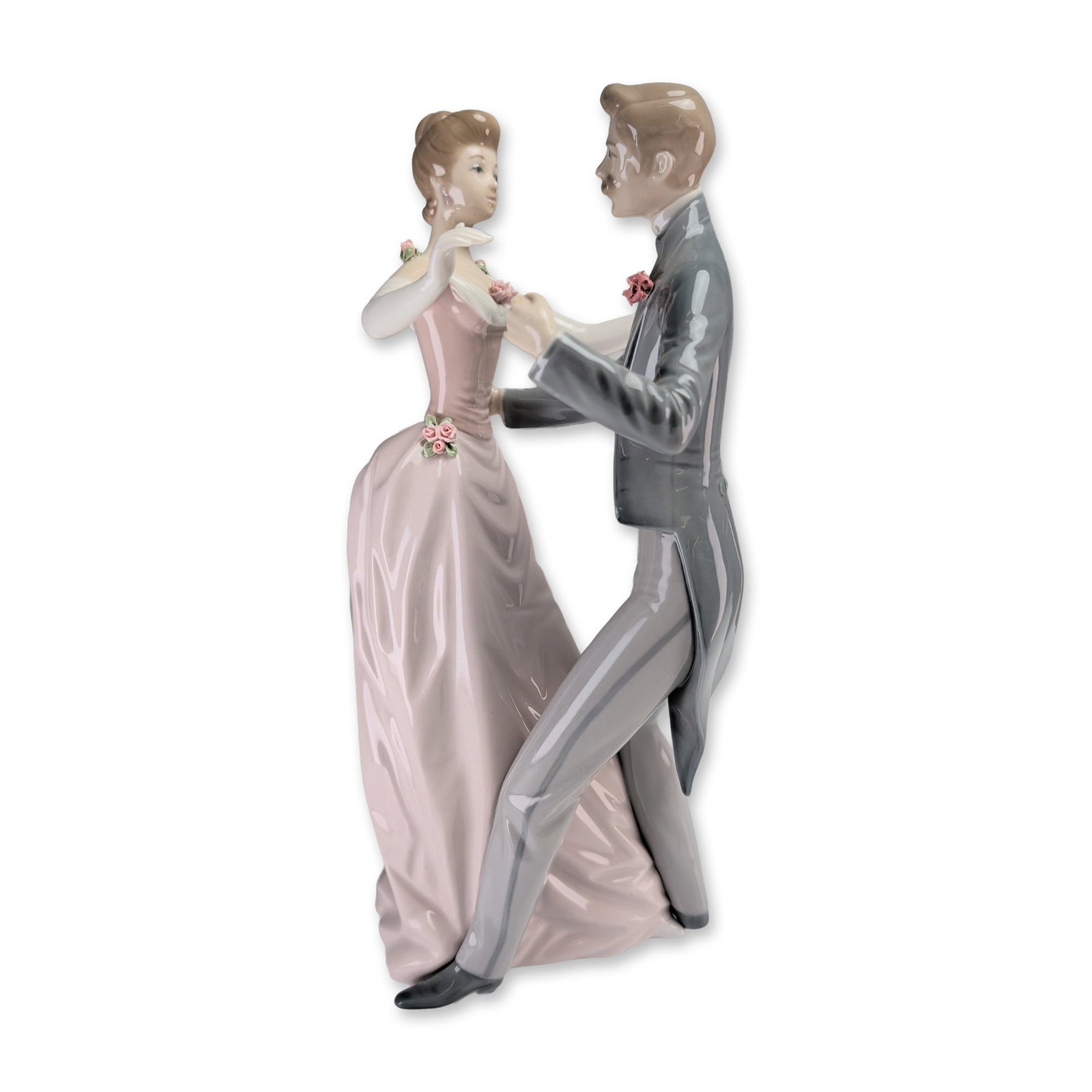 Lladro Porcelain Sculpture, Anniversary Waltz 1001372: Designed by Antonio Ballester. The piece depicts a couple in a dancing pose, featuring a man in a grey tuxedo with a tailcoat and a woman in a sleeveless pale pink gown. The dress is accented with sma