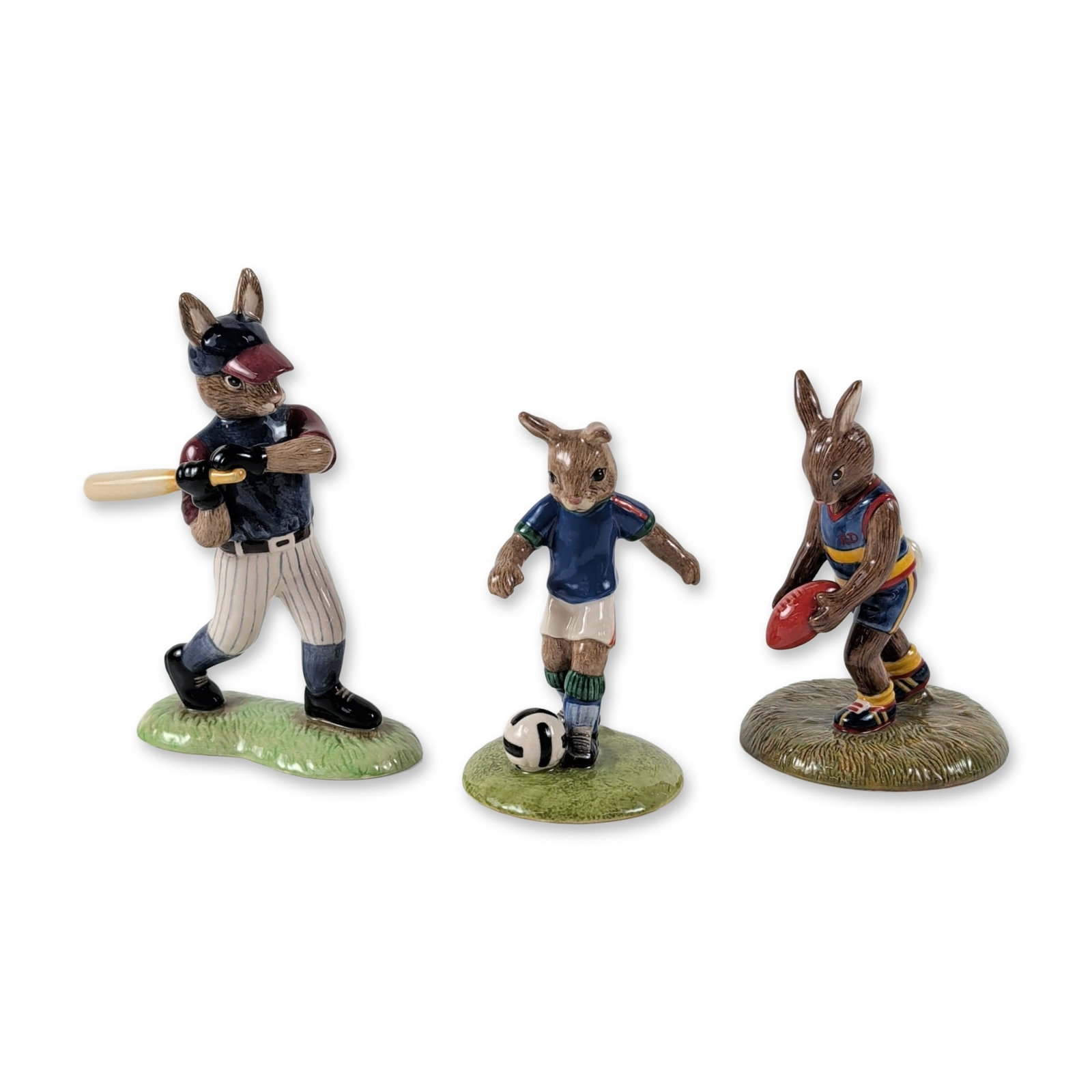 3pc Royal Doulton Bunnykins Sports Figurines: Trio of Royal Doulton Bunnykins hand-decorated earthenware figurines, each depicting a rabbit participating in a different sport. The set comprises Aussie Rules Bunnykins (DB 508), Soccer Bunnykins (D