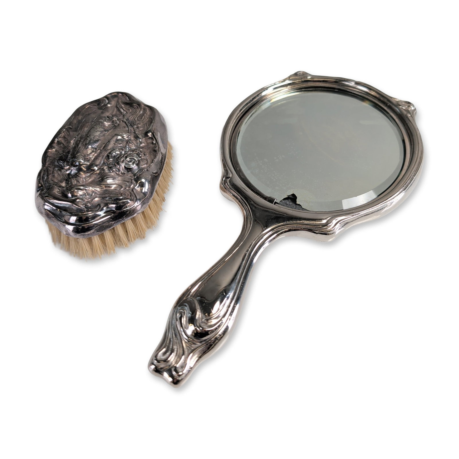 2pc Art Nouveau Style Silver Toned Vanity Set: Art Nouveau style vanity set comprising a hand mirror and hairbrush. The set is constructed from silver-toned metal with ornate repousse decoration featuring a stylized female figure with long, swirli