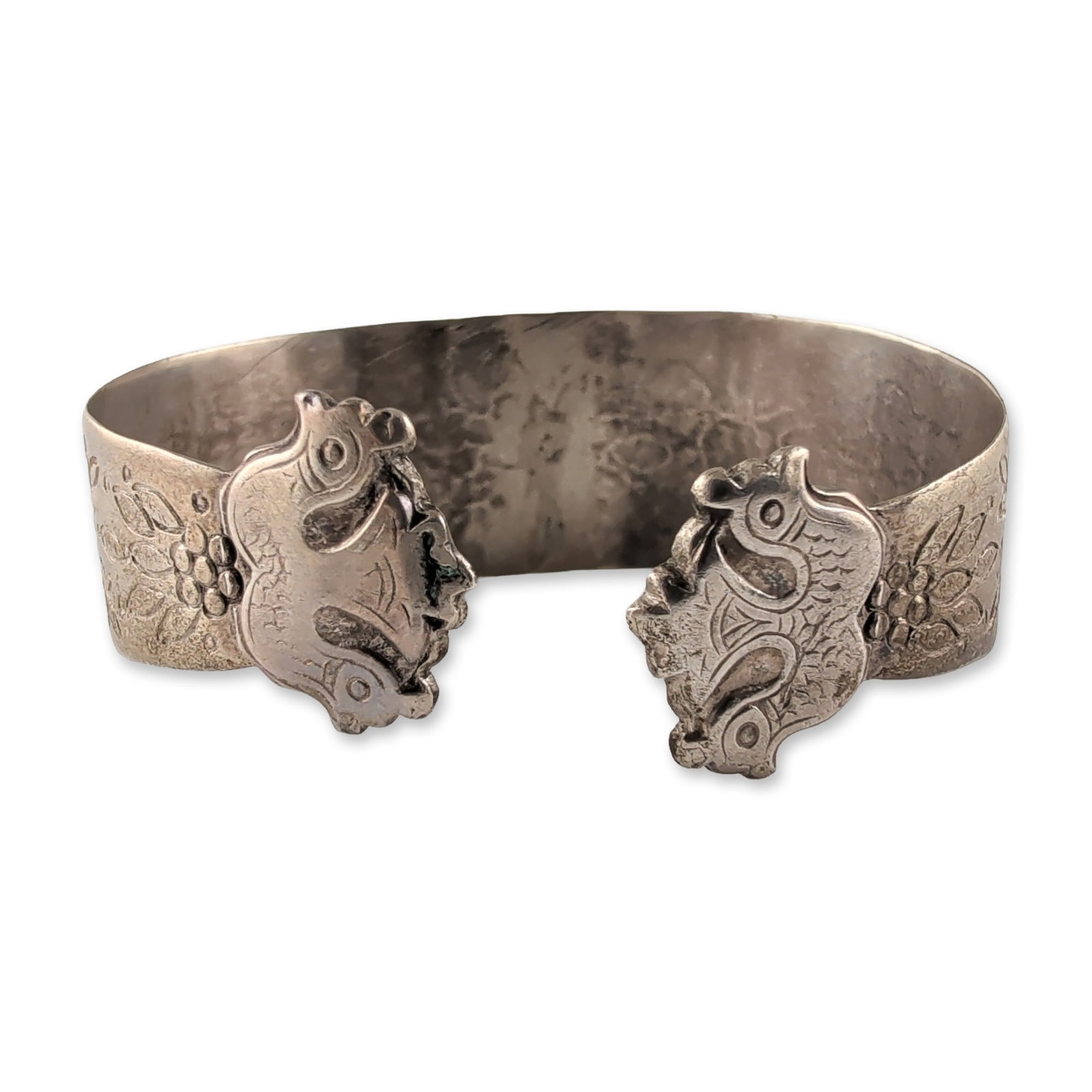 Southeast Asian Folk Art Style Sterling Silver Cuff Bracelet: Featuring intricate chased and repousse ornamentation. The band is decorated with floral and foliate motifs against a stippled background. The terminals are fashioned into stylized bird heads meeting