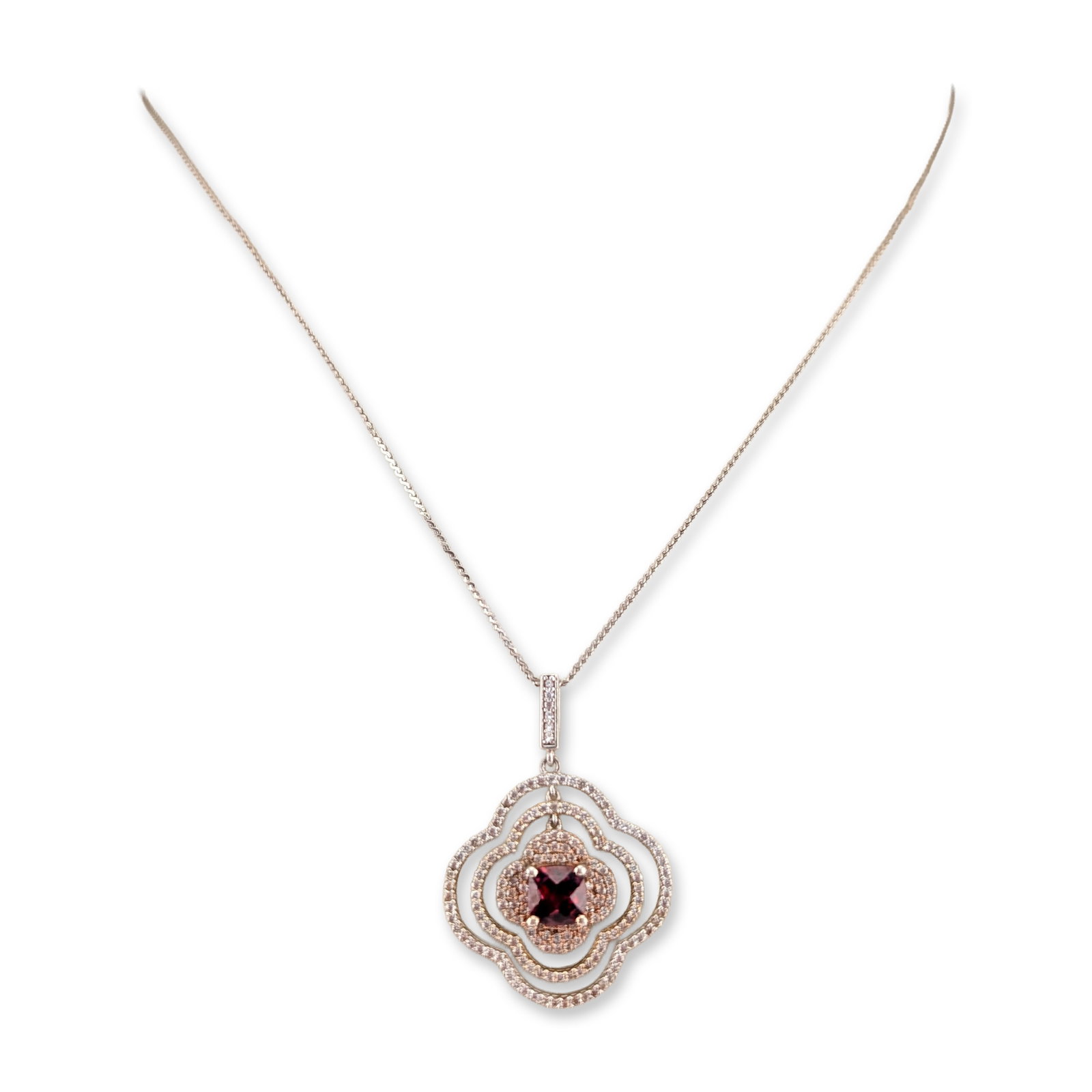 Sterling Silver and Garnet Quatrefoil Pendant Necklace: A pendant necklace in sterling silver featuring a multi-tiered quatrefoil pendant. The central feature is a square cushion-cut faceted garnet, surrounded by three concentric clover-shaped tiers. Each 