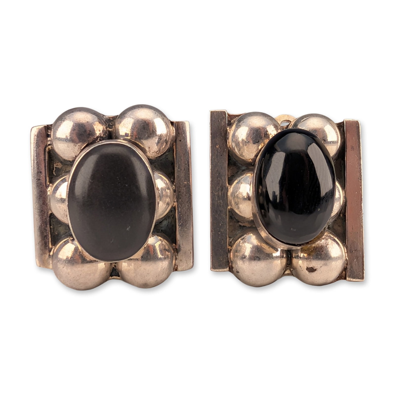 Pair of Taxco Sterling Silver and Black Onyx Clip Earrings: Pair of Taxco modernist clip-on earrings in sterling silver, each featuring a central oval black onyx cabochon. The gemstones are bezel-set and surrounded by six polished silver spheres, flanked by tw