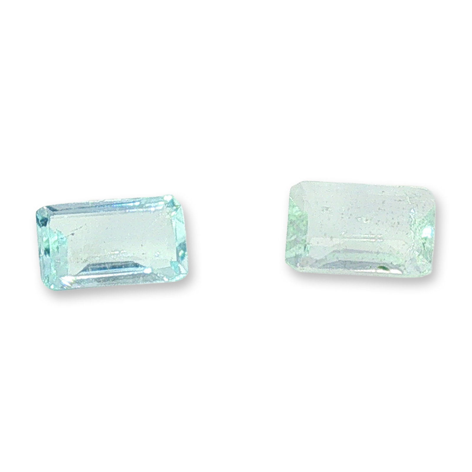 2pc Rectangular Cut Loose Aquamarine Gemstones: Pair of loose gemstones appearing with an aquamarine-like hue and featuring a rectangular step-cut with clipped corners. The stones exhibit a soft, light blue and pale greenish-blue color. Internal in