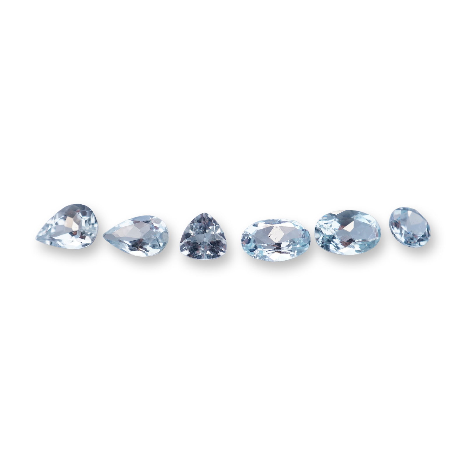 Group of Six Faceted Aquamarine Gemstones: An assortment of faceted aquamarine gemstones presented in a variety of shapes. The collection includes two pear shapes, one trillion cut, two oval cuts, and one round brilliant cut. Each stone