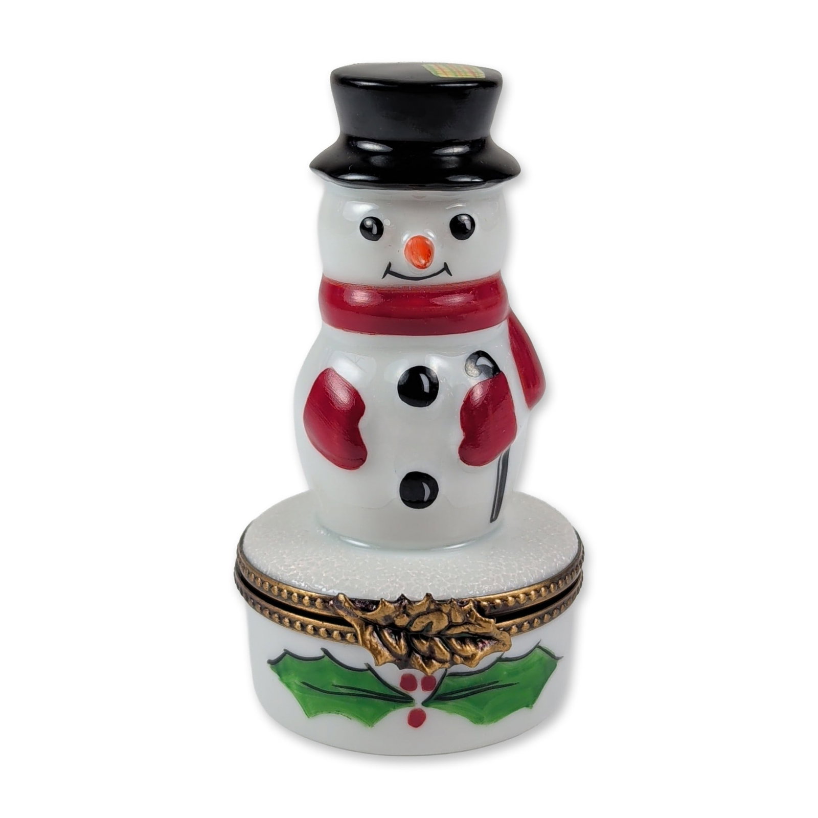 Limoges Snowman Porcelain Trinket Box: La Gloriette Limoges hand-painted porcelain trinket box in the form of a snowman. The figurine features a glazed white body with a black top hat, red scarf, and red mittens, standing on a textured whi
