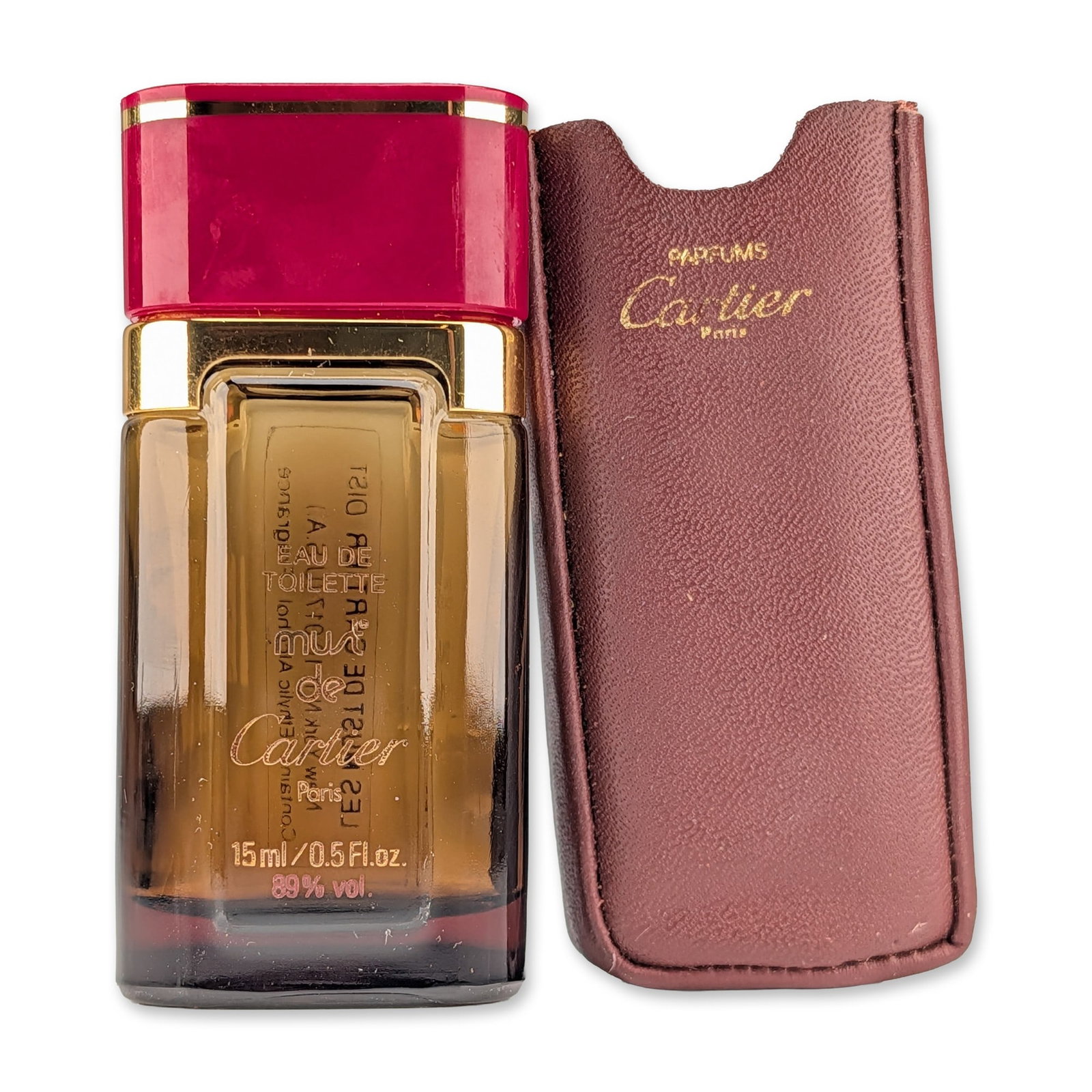 Cartier Vintage Must de Cartier Eau de Toilette Bottle and Case: Vintage Cartier travel bottle for Must de Cartier Eau de Toilette. Rectangular amber glass bottle with a gold-toned metal collar and a burgundy plastic cap featuring a gold-toned accent band. The fron