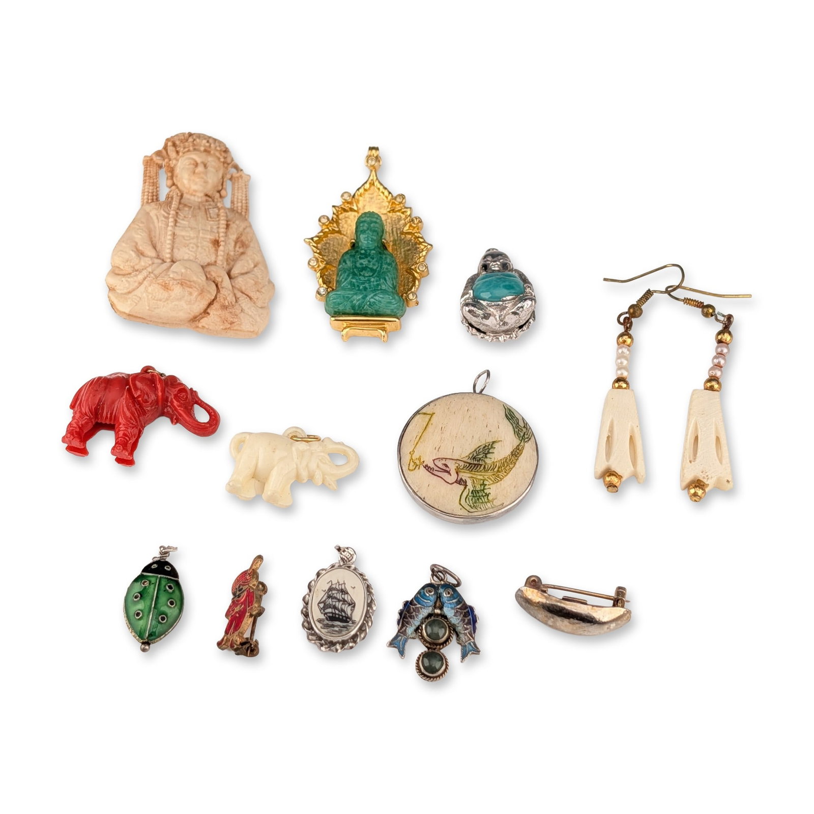 12pc Collection of Figurative and Enameled Jewelry: An assortment of jewelry featuring various cultural and animal motifs. The group consists of two brooches, eight pendants and charms, one pin, and a pair of earrings. Included is a large carved cream-