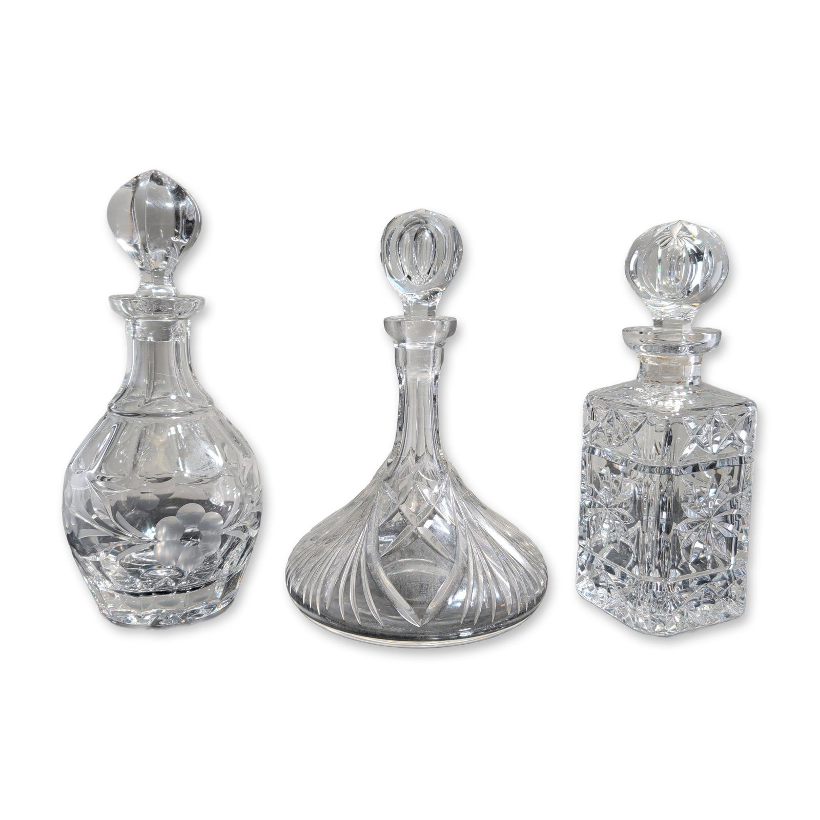 3pc Crystal Decanters with Stoppers: A trio of cut lead crystal decanters in square, ship's, and bulbous forms. The square-section decanter is decorated with deep diamond-point and starburst cuts and a faceted globular stopper. The ship'