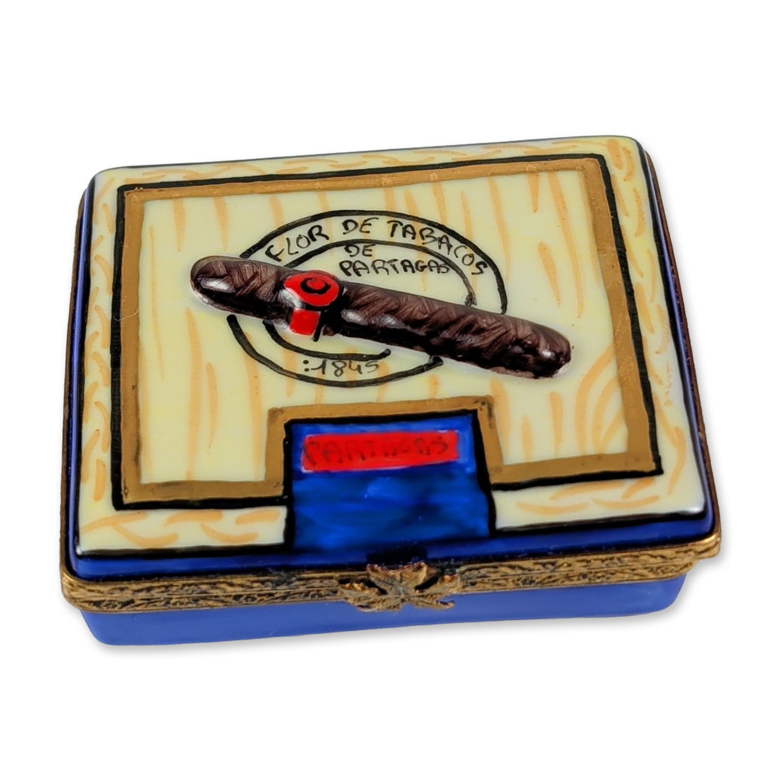 French Limoges Hand Painted Cigar Trinket Box: A French hand-painted porcelain trinket box fashioned in the form of a Partagas cigar box. The exterior lid features a faux-bois finish decorated with a single painted cigar and the Flor de Tabacos de