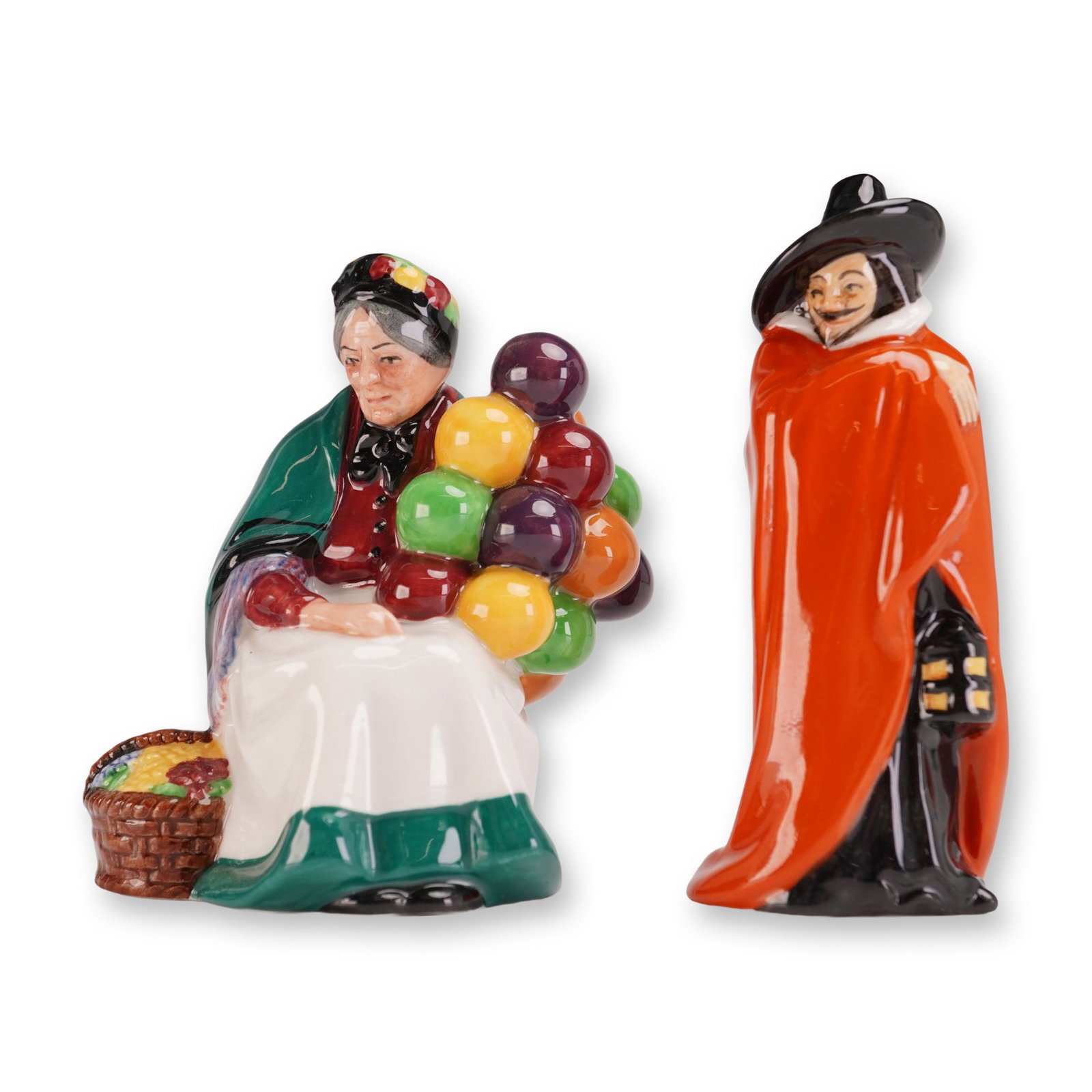 2pc Royal Doulton Figurines, Guy Fawkes (HN3271) and The Old Balloon Seller (HN2129): Hand painted figures. One figure is Guy Fawkes in a long red cloak and black wide brim hat, shown holding a lantern. The other figure is a seated woman selling colorful balloons. Each marked Royal Dou