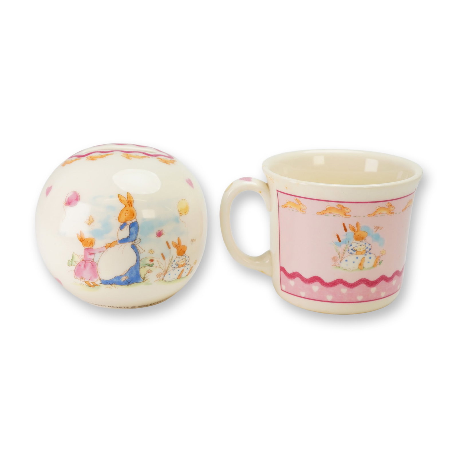 2pc Royal Doulton Bunnykins Bone China Money Ball and Mug: This set of Royal Doulton Bunnykins nursery ware is presented in the Sweetheart pattern, identified by the reference H5317. The collection comprises a spherical bone china money ball and a single-hand