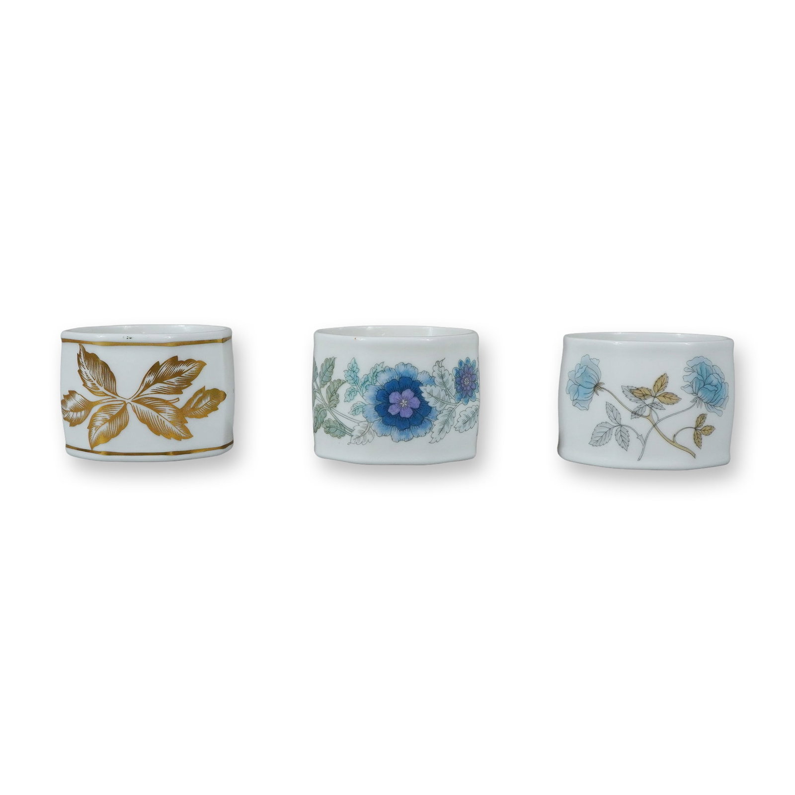 3pc Wedgwood Bone China Napkin Rings: A trio of English bone china napkin rings produced by Wedgwood. Each ring features a faceted octagonal exterior and a smooth cylindrical interior. The group includes three distinct patterns. One ring 