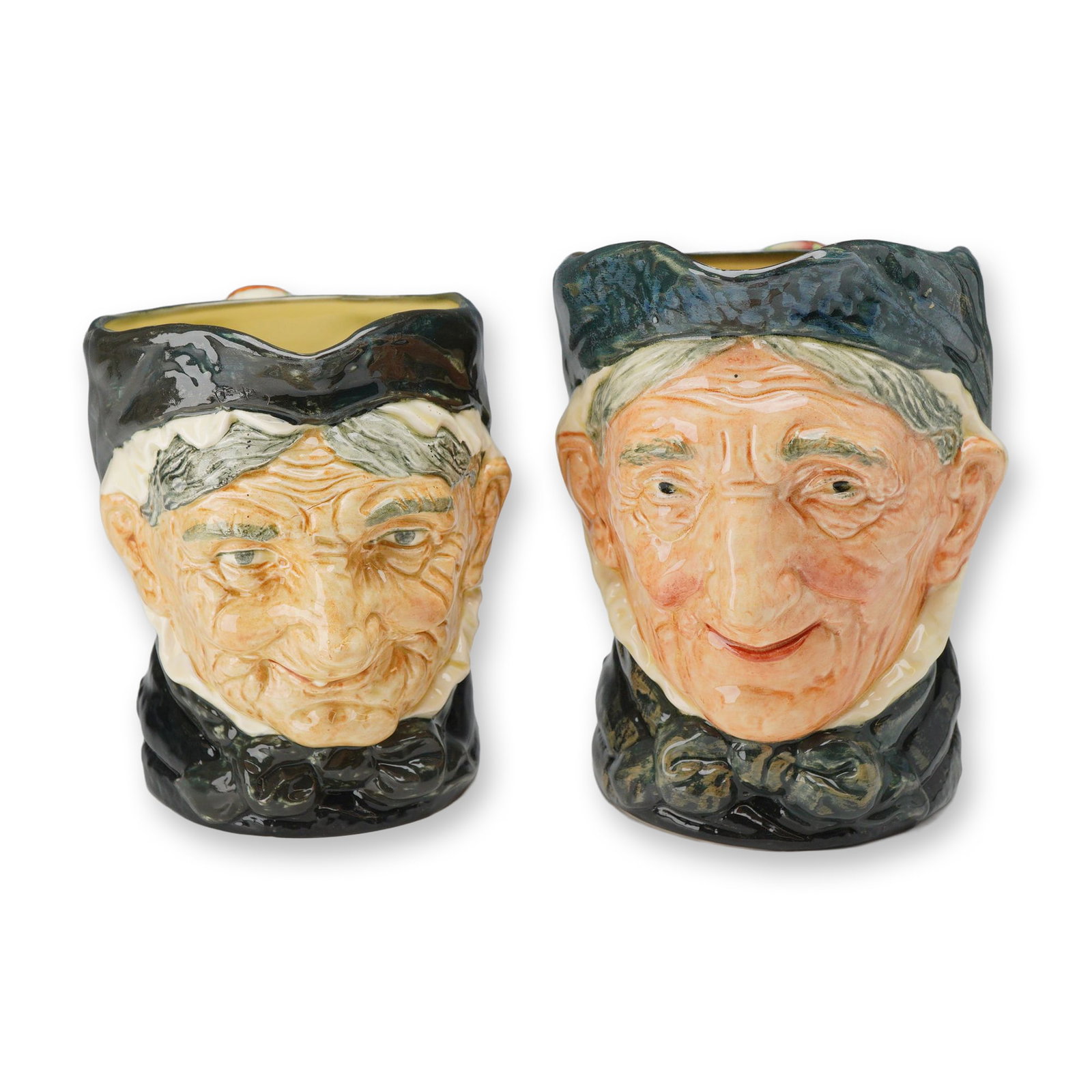 Pair of Royal Doulton Large Character Jugs, Granny and Granny Toothless (D5521): A pair of character jugs in glazed earthenware, modeled by Harry Fenton as the Granny character. Each jug depicts an elderly woman wearing a bonnet with a hand-painted multi-color striped shawl-wrappe