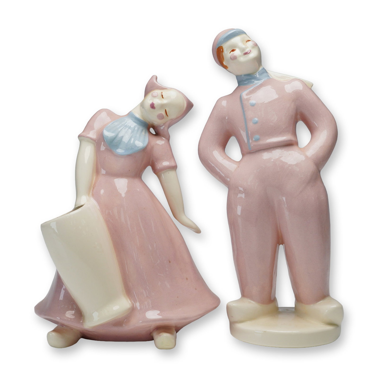 Pair of Heidi Schoop Art Creations Ceramic Figurines, Dutch Boy and Girl: Each figure is hand-painted in soft pastel pink with light blue accents. The boy is shown standing with hands on hips, wearing a cap, scarf, and trousers, while the girl wears a traditional dress and 