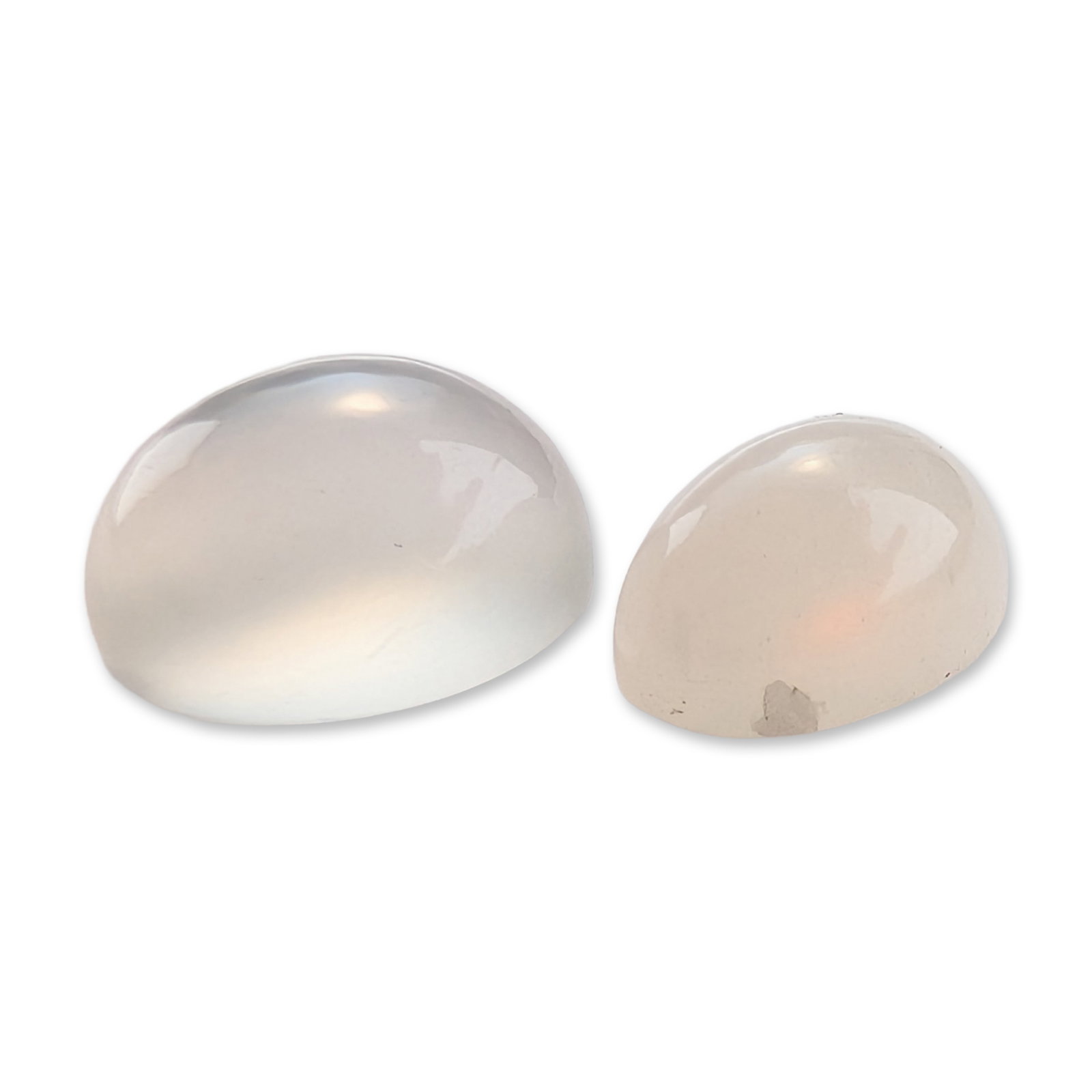Two Moonstone Cabochon Gemstones: Two loose oval cabochon moonstone gemstones. The larger stone is translucent with a silvery-blue adularescent sheen and characteristic internal fractures. The smaller stone exhibits a milky white