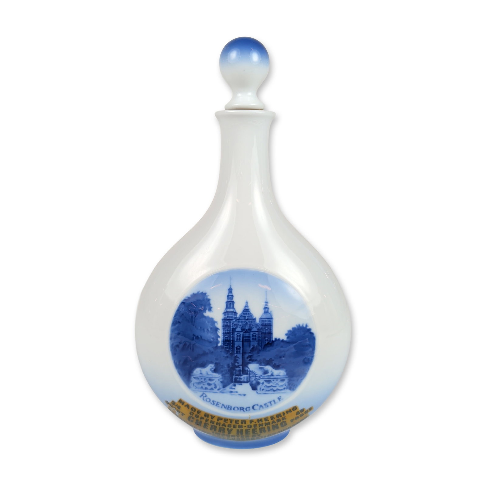 Royal Copenhagen Porcelain Rosenborg Castle Cherry Heering Decanter: A Danish porcelain liquor decanter featuring a bulbous body tapering to a narrow neck, accompanied by a matching ball-shaped stopper. The vessel is decorated with a blue-to-white ombre gradient at