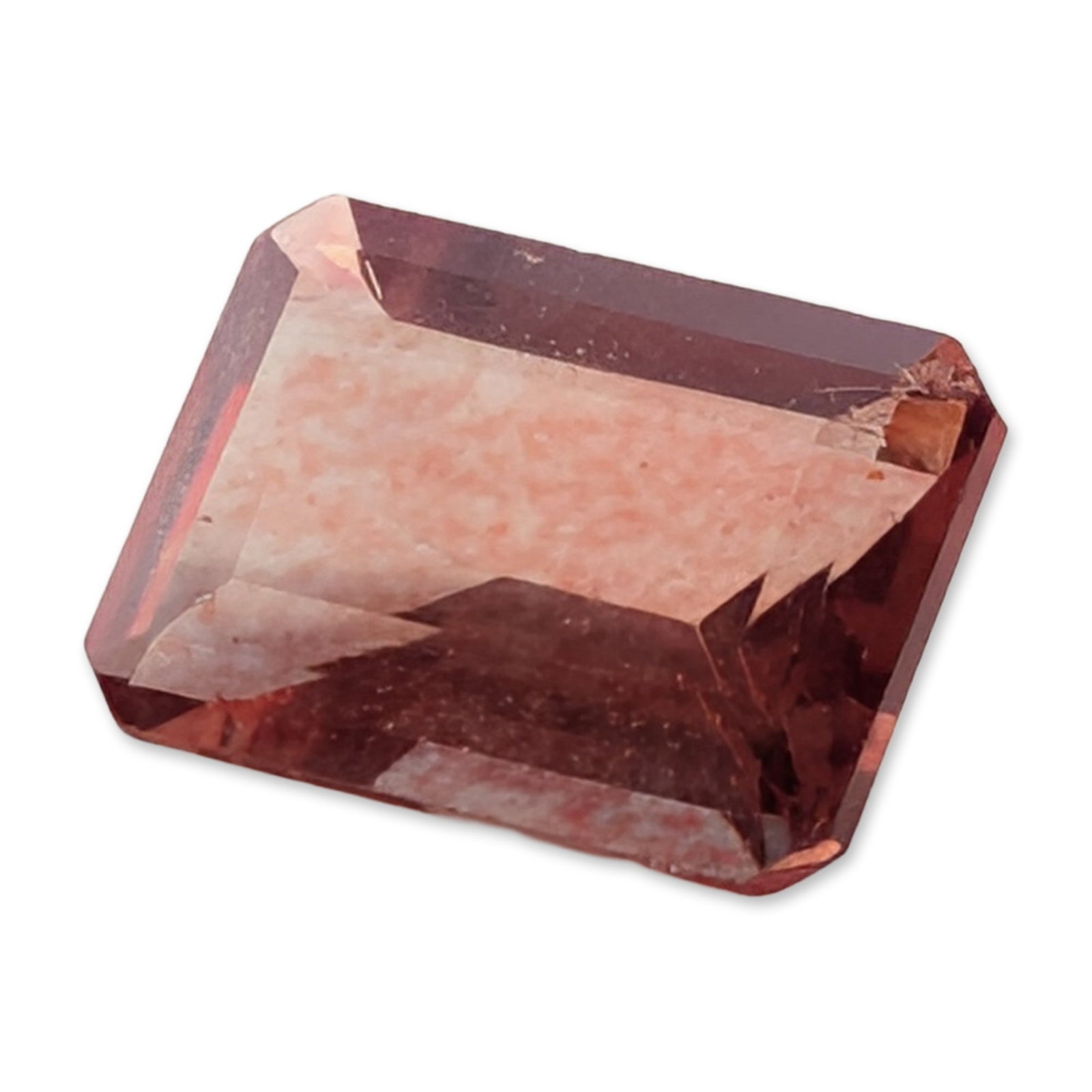 Loose Emerald Cut Pinkish-Red Stone: Loose faceted stone fashioned in an emerald cut with truncated corners. The stone exhibits a saturated pinkish-red hue with deep magenta tones throughout. The body of the stone features prominent inte