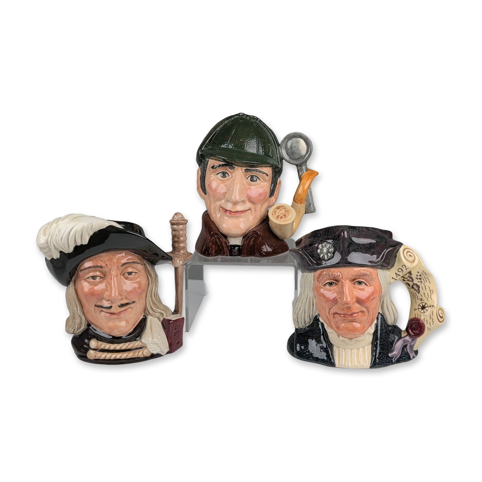 3pc Royal Doulton Large Character Jugs, Aramis (D6441), The Sleuth (D6631), and Christopher Columbus: A group of three English Royal Doulton glazed ceramic character jugs depicting fictional and historical figures. The first depicts Aramis from The Three Musketeers, wearing a wide-brimmed black hat wi