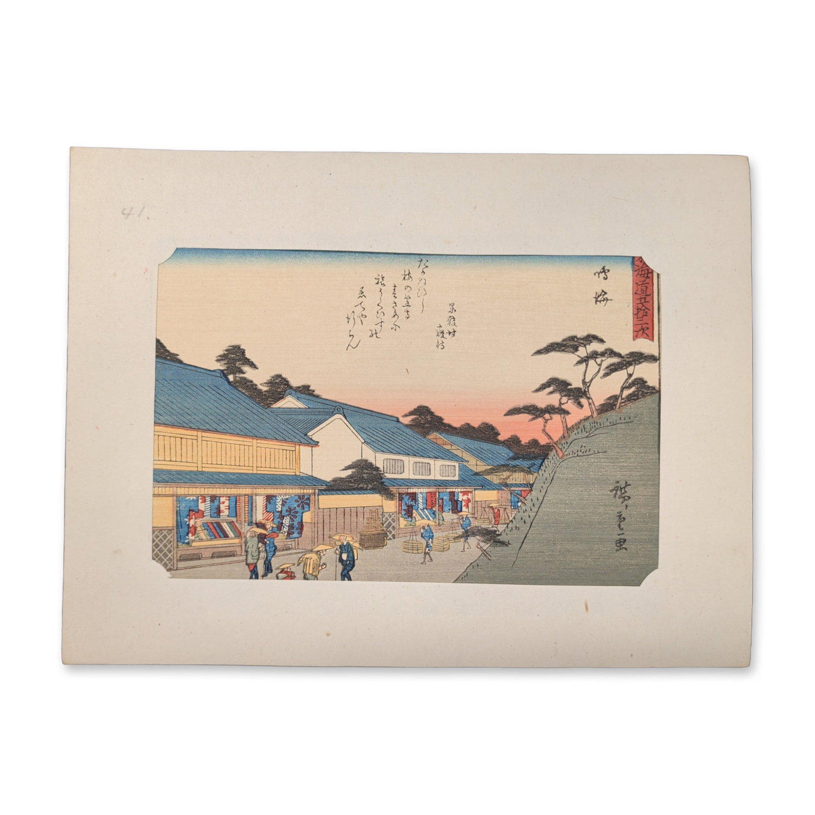 After Utagawa Hiroshige (Japanese 1797-1858) Narumi: From a Fifty-three Stations of the Tokaido: A line of pack horses and traveling merchants passes a prominent, deep-blue roofed textile shop showcasing traditional local shibori fabrics. Everyday townspeople and shoppers navigate the street betw