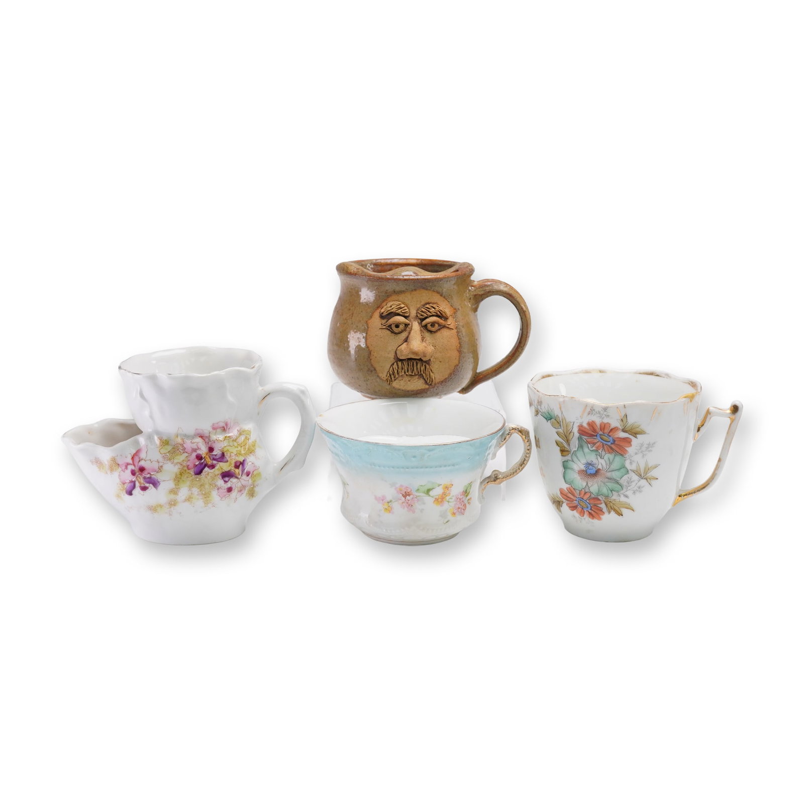 4pc Assorted Antique Moustache Cups and Shaving Cup: Collection of four late 19th to early 20th century cups including three moustache cups, one with gilt inscription and floral decoration, one with a blue band and floral motifs, and a brown pottery nov