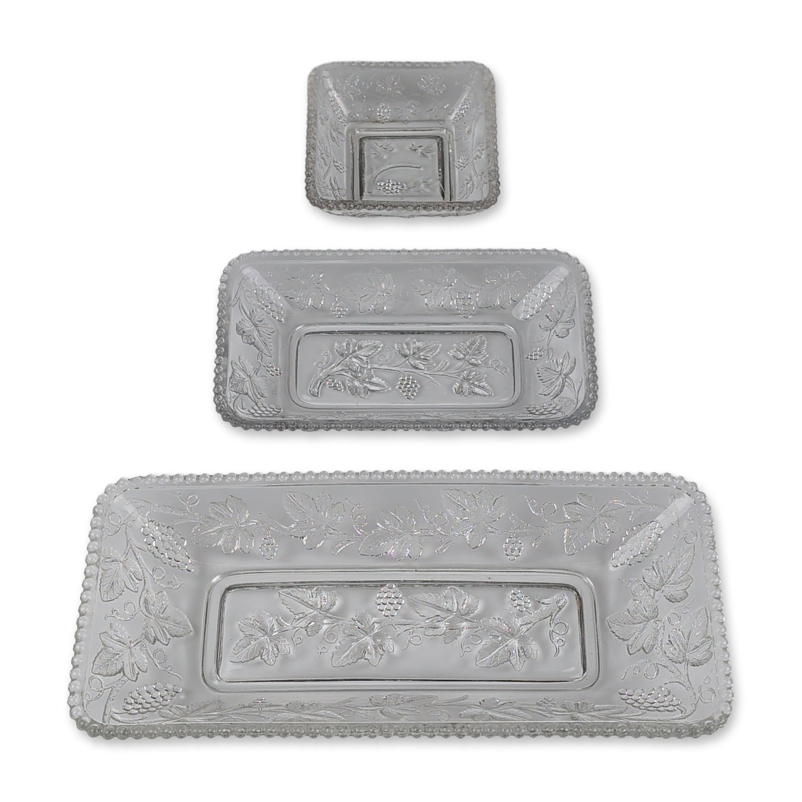 3pc Indiana Glass Harvest Grape Nested Trays: Trio of nesting trays in clear pressed glass, featuring the Harvest Grape pattern. The set includes one large rectangular tray, one medium rectangular tray, and one square bowl, all decorated with emb