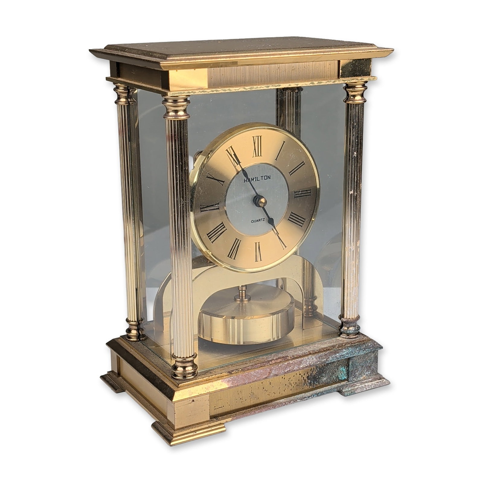 Hamilton German Quartz Brass and Glass Mantel Clock: Hamilton anniversary-style mantel clock in gold-tone metal and glass, featuring a rectangular case with four fluted corner pillars and a stepped base. The circular dial presents a gold-tone chapter ri