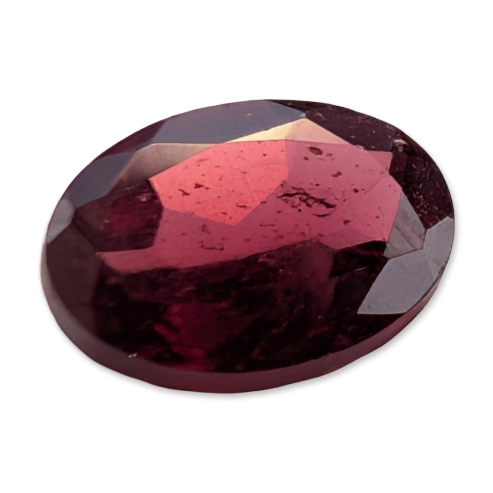 Oval Faceted Purplish-Red Garnet Gemstone: A loose faceted garnet gemstone in a deep purplish-red hue. The stone features an oval mixed cut with a brilliant-style crown and faceted pavilion. The color is saturated with a raspberry tone and not