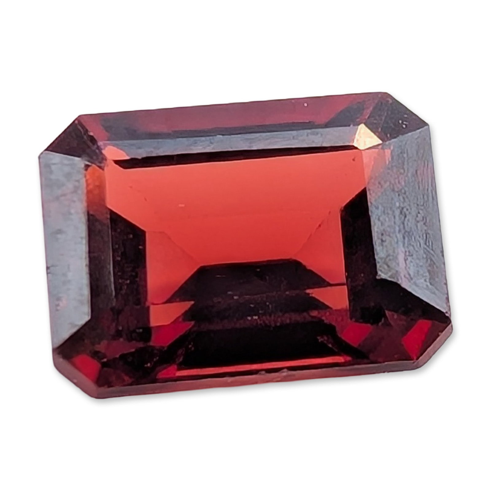 Emerald Cut Red Garnet Gemstone: Loose gemstone, emerald cut, which appears to be a natural red garnet. The stone displays a deep, saturated red color with visible internal inclusions and facet extinction. It is an octagonal step cut