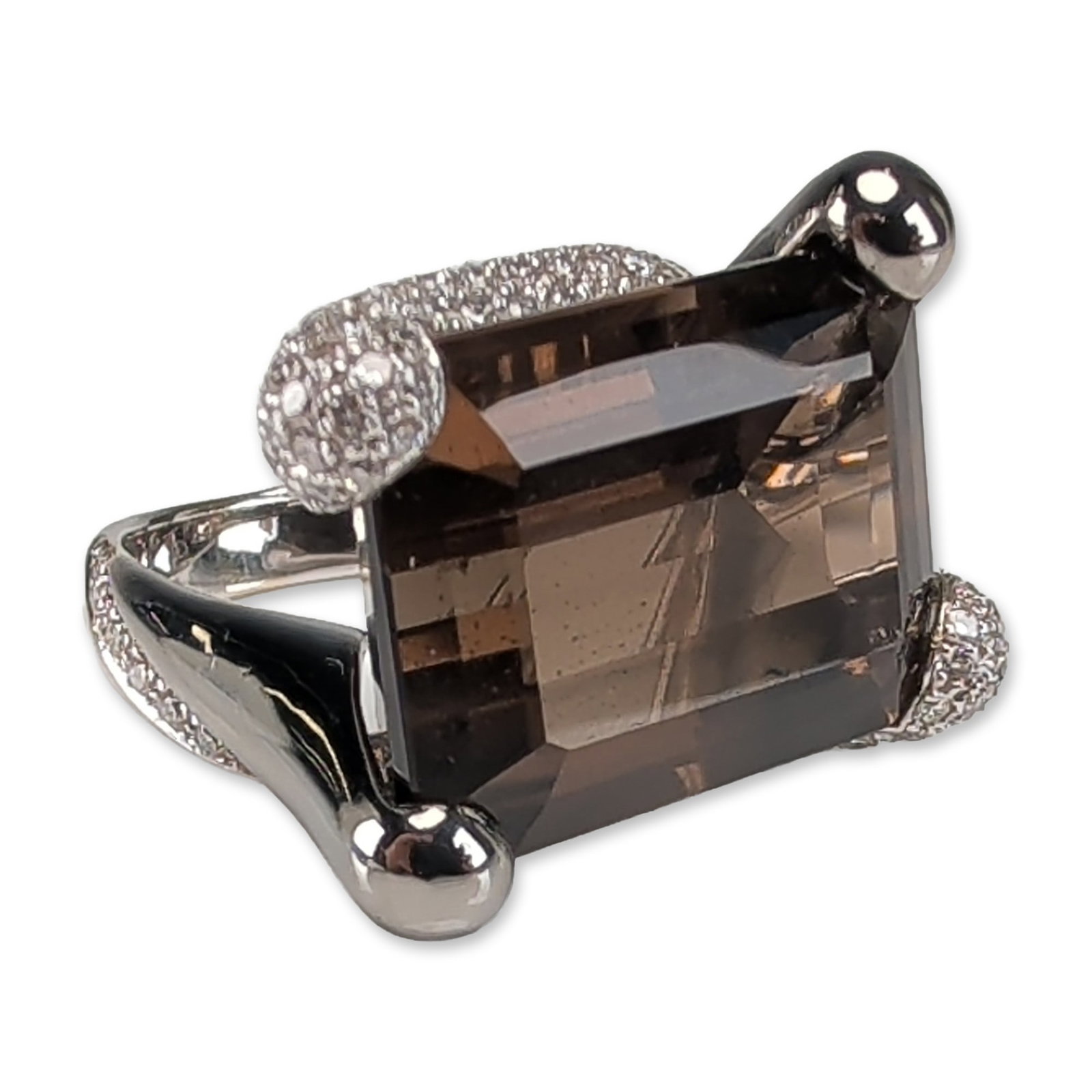 18K White Gold 25ct Smoky Quartz & Diamond Cocktail Ring: Featuring a 25 carat weight emerald-cut smoky quartz center stone set in a modern, asymmetrical East-West (E-W) 18K white gold diamond band. The design incorporates four spherical prongs, with two hig