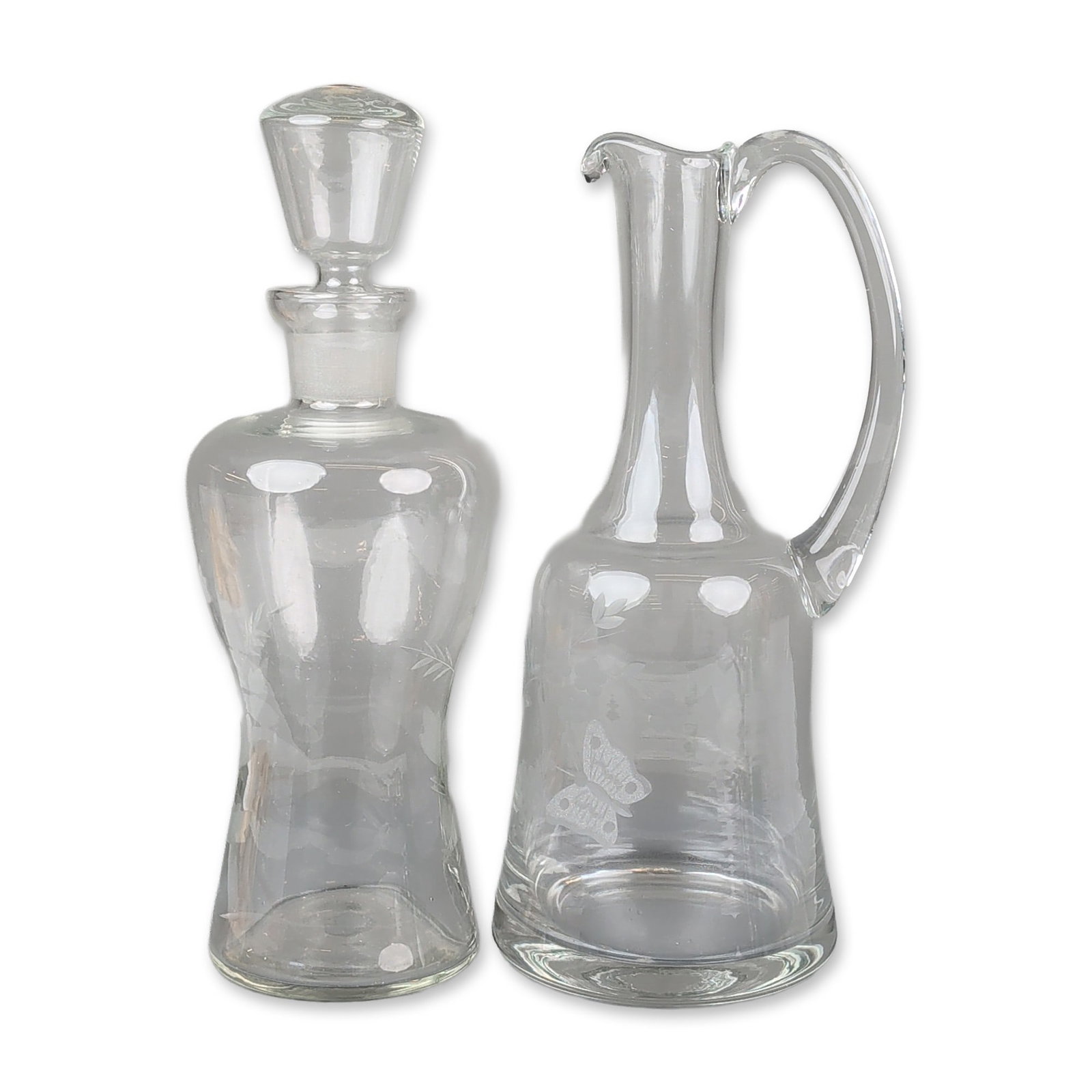 2pc Floral Pattern Glass Decanters: A two-piece group of clear glass decanters. One decanter features a slender neck, a pulled spout, and an applied loop handle, decorated with a wheel-engraved butterfly and floral sprigs. The hourglass